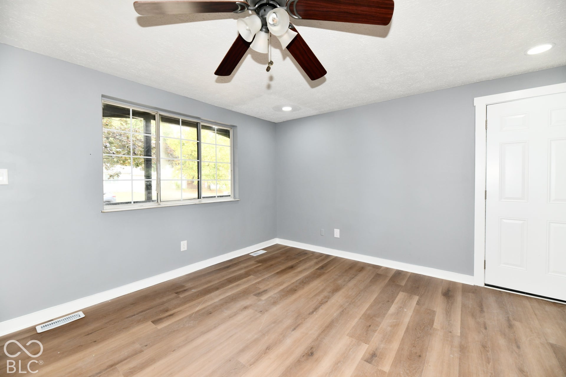 Room featuring wood-finish flooring, a multi-pane sliding window, a six-panel door, and a ceiling fan with integrated lighting