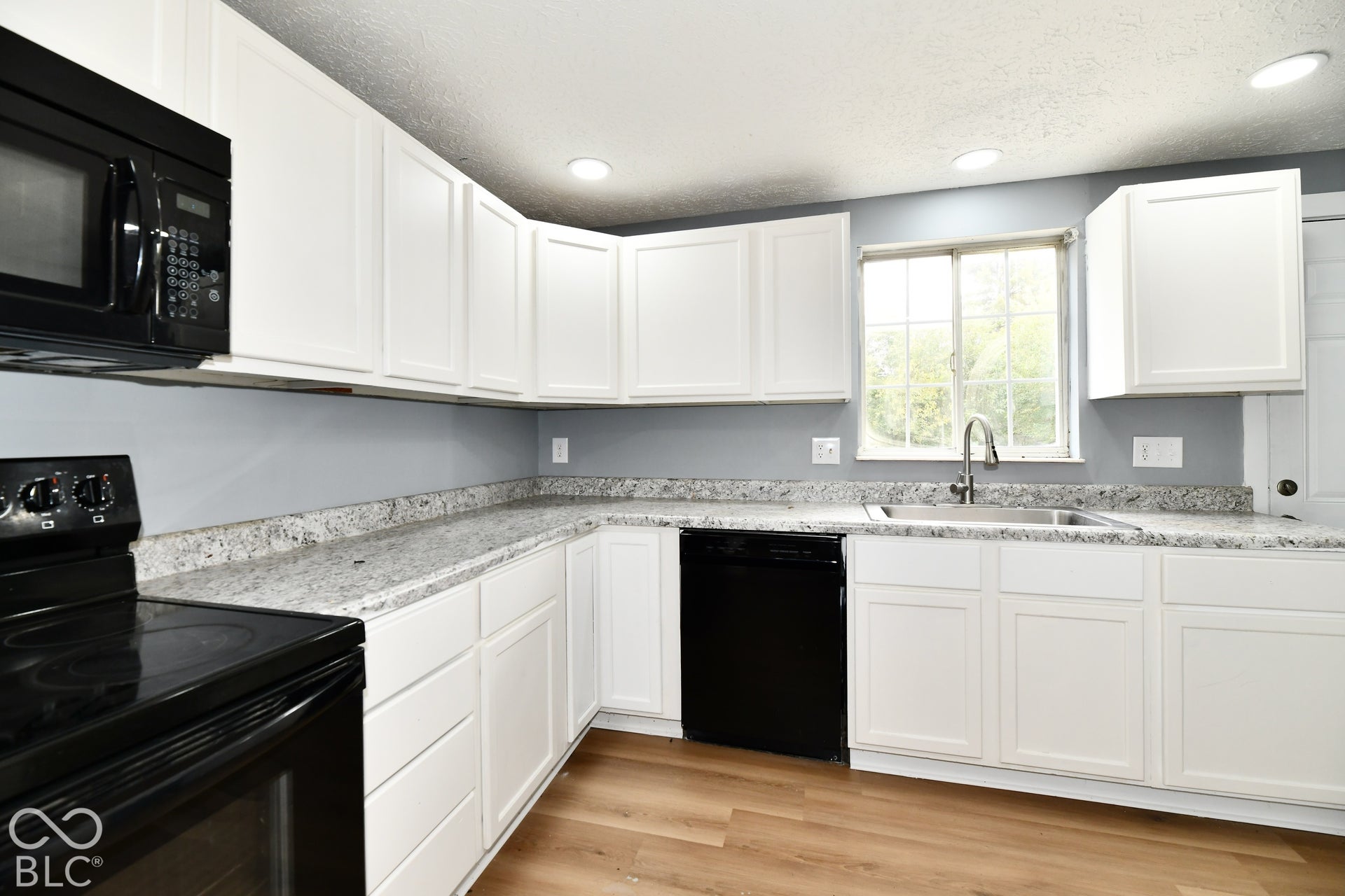 Kitchen featuring white shaker-style cabinetry, stone-finish countertops, black appliance suite, undermount sink with a gooseneck faucet, and wood-finish flooring