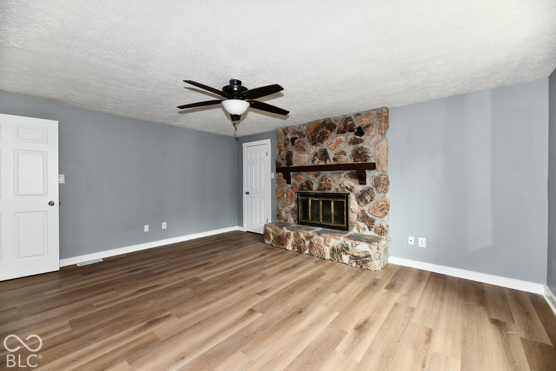 Interior space featuring wood-finish flooring, floor-to-ceiling natural stone fireplace, dark wood mantel, and ceiling fan with integrated lighting