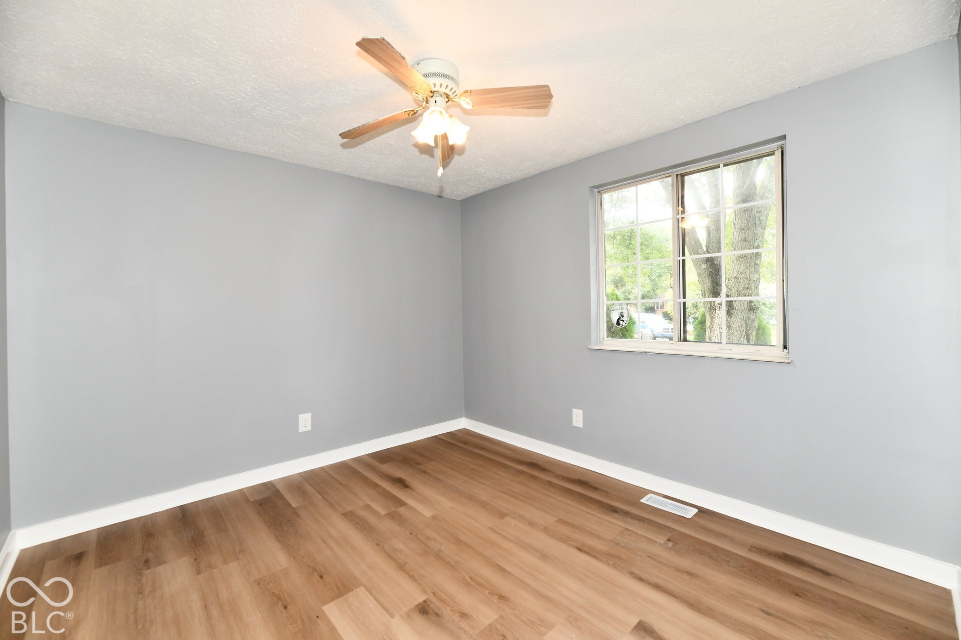 Neutral-toned interior space featuring wood-finish flooring, a multi-pane window, and a ceiling fan with integrated lighting