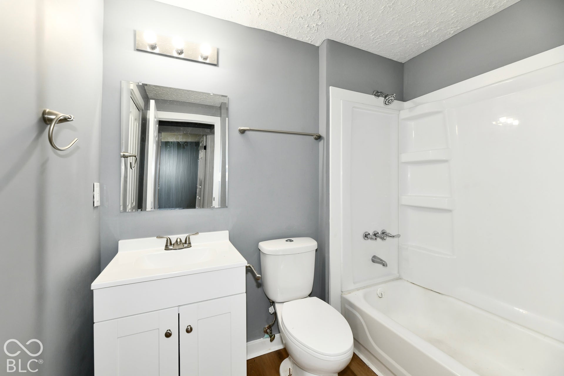 Bathroom featuring a white vanity cabinet, integrated sink, three-light vanity fixture, wall-mounted mirror, and a combination tub and shower surround