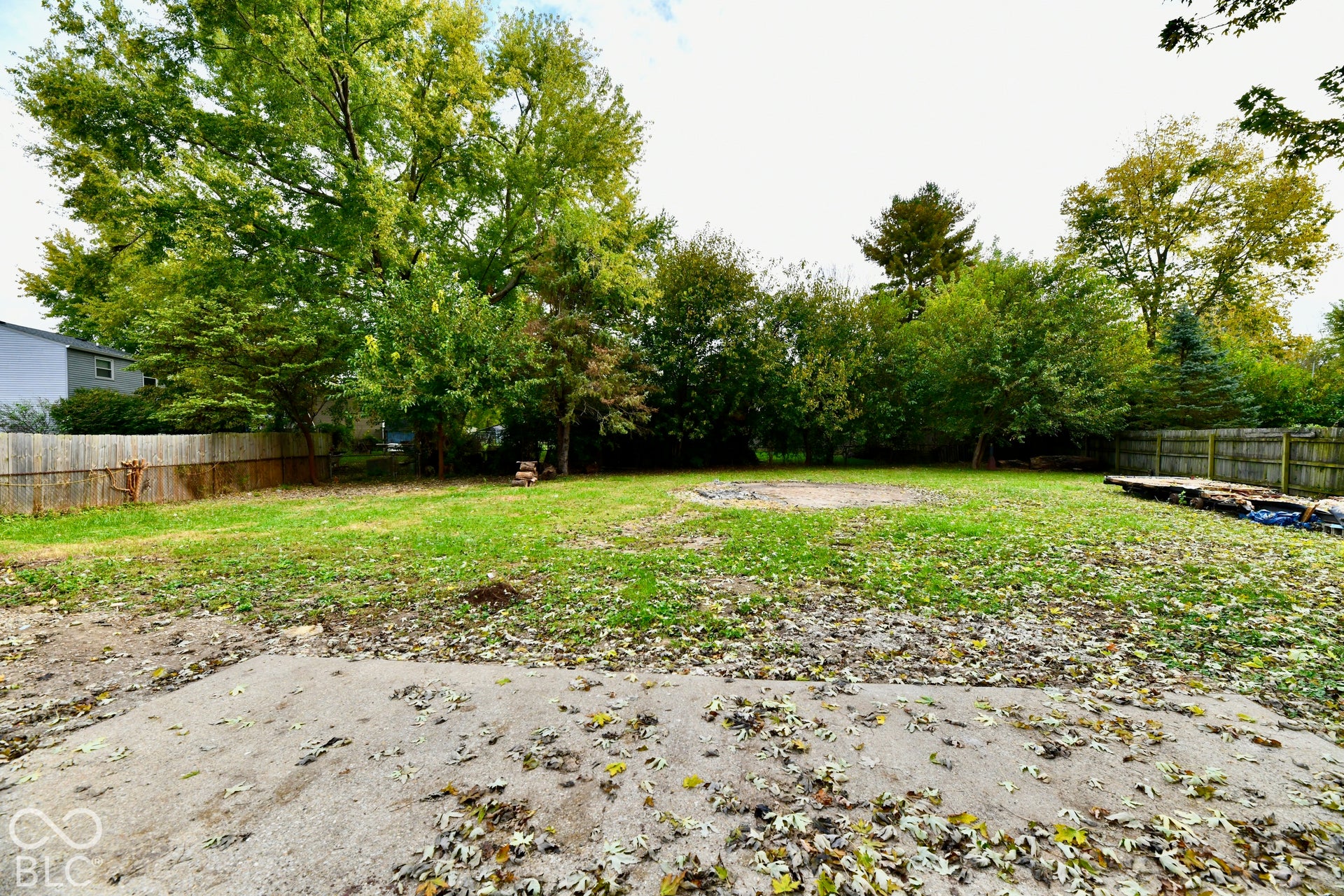 Expansive backyard featuring a concrete patio, perimeter wood fencing, and mature trees