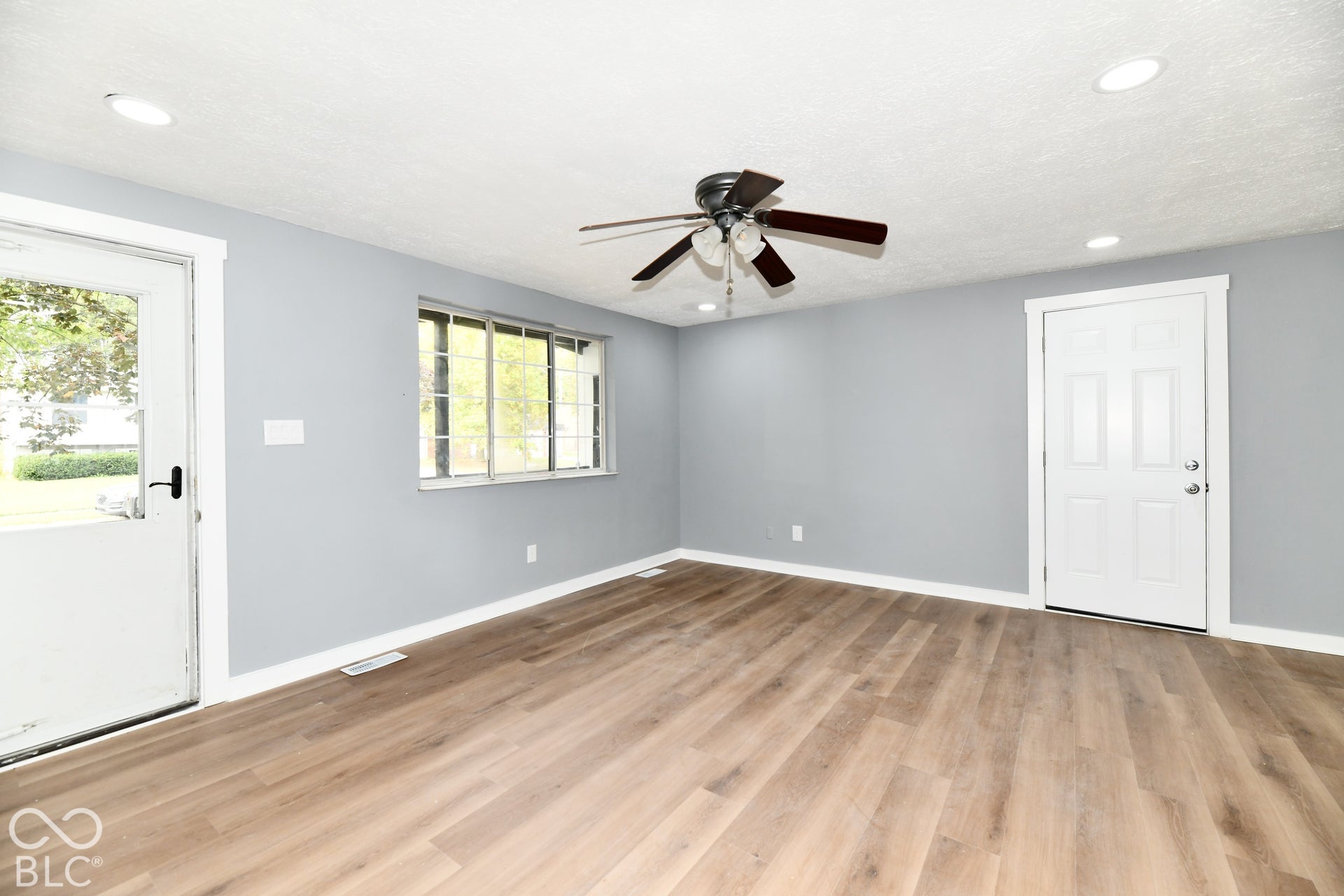 Interior room featuring wood-finish flooring, recessed lighting, a central ceiling fan with integrated light fixture, a glass-panel exterior door, and a multi-pane window