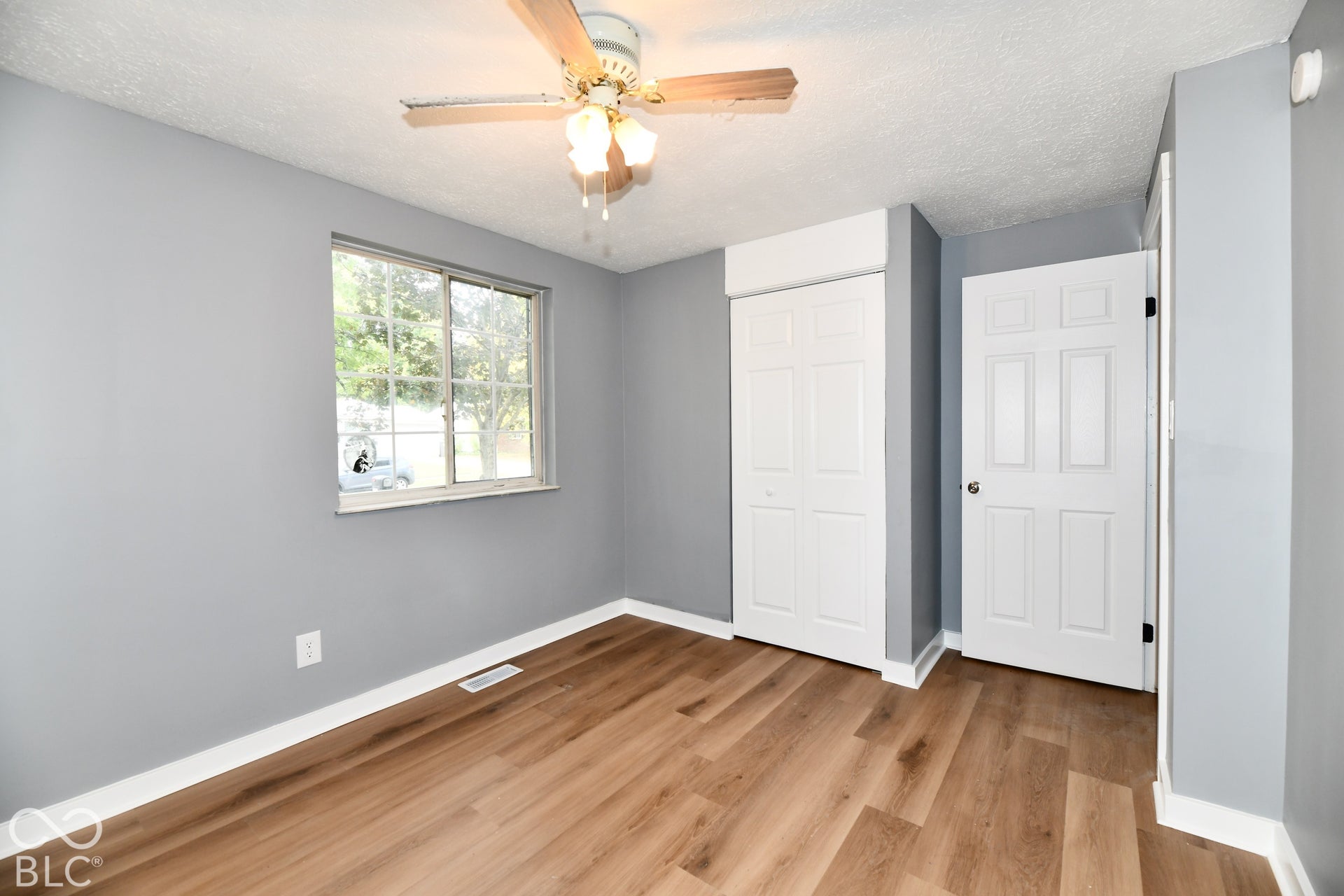 Room featuring wood-finish flooring, a ceiling fan with integrated lighting, a sliding door closet, and a multi-panel interior door