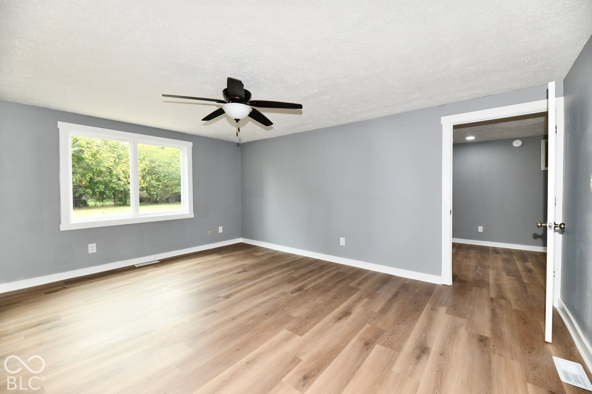 Neutral-toned interior space featuring wood-finish flooring, a multi-pane window, and a central ceiling fan with an integrated light fixture