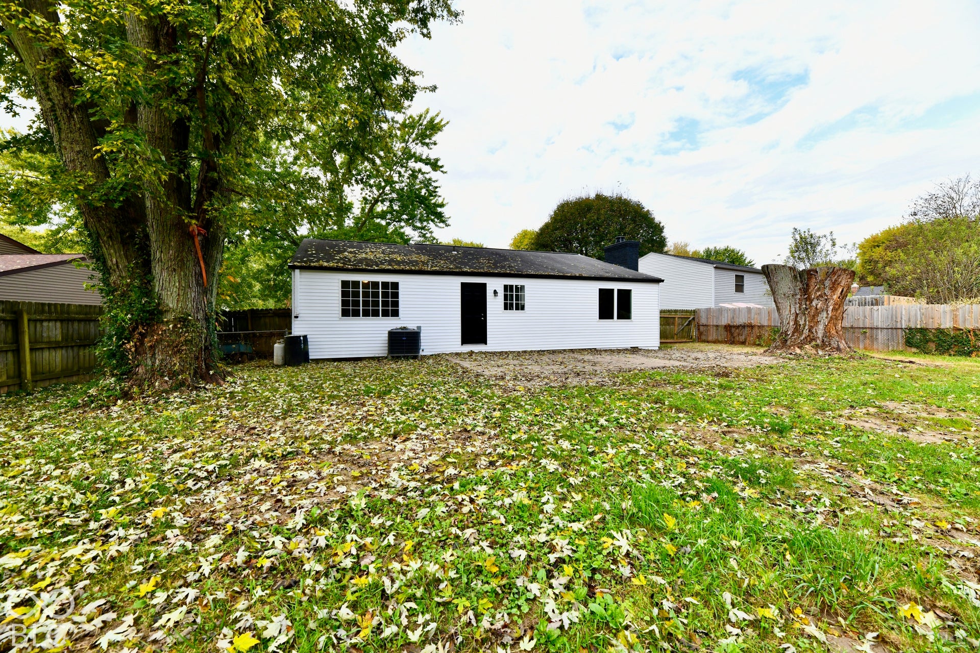 Backyard featuring white horizontal siding, grid-pattern windows, wood privacy fencing, mature trees, and a concrete patio