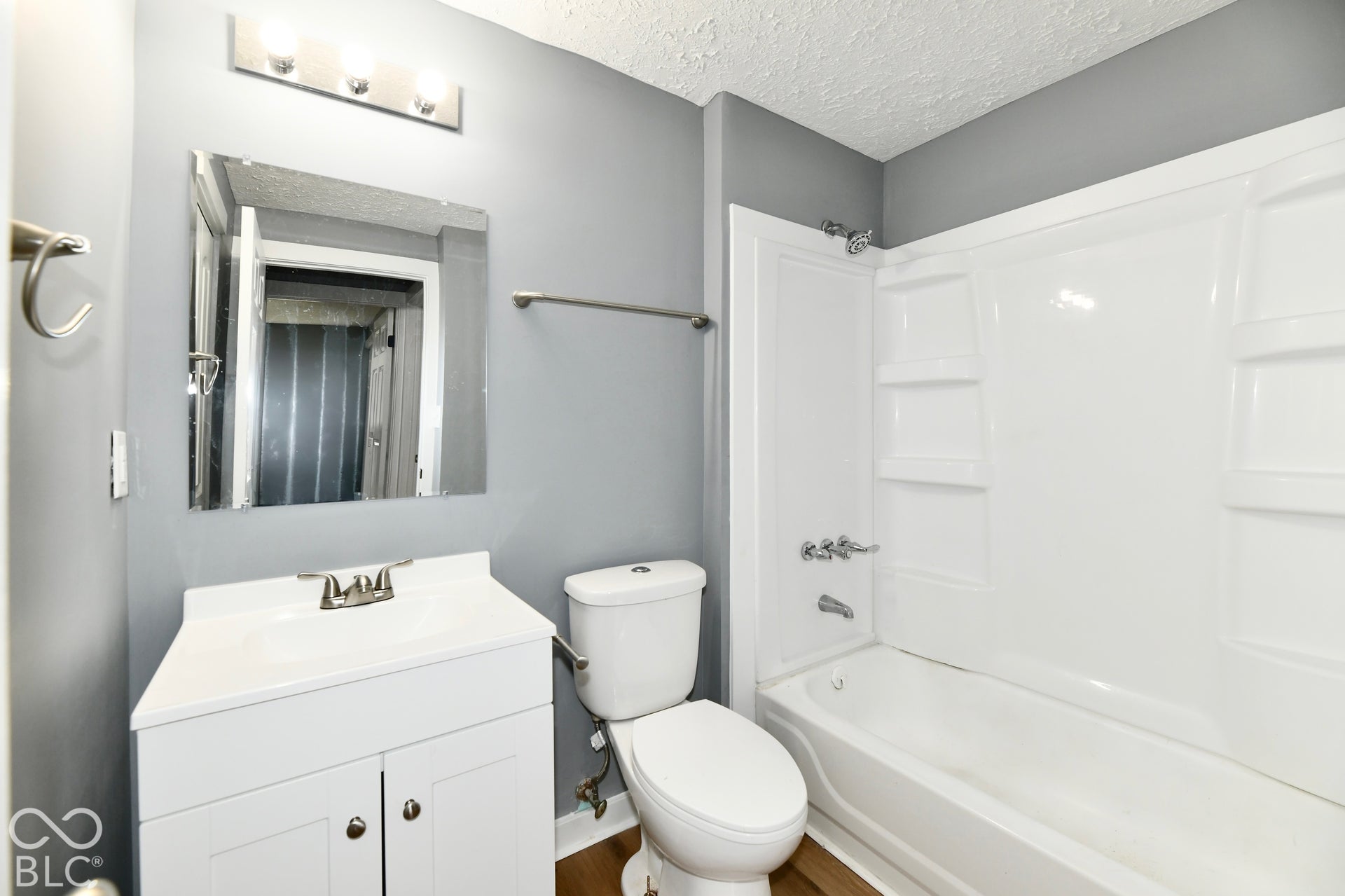 Bathroom featuring a white vanity cabinet, a wall-mounted vanity mirror, a three-light fixture, and a white acrylic tub-and-shower surround with integrated shelving