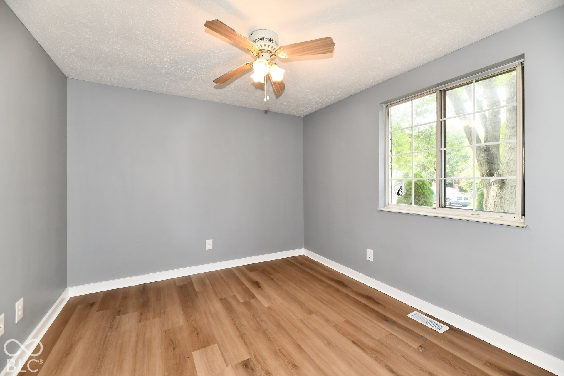 Room featuring wood-finish flooring, a multi-light ceiling fan, and a grid-pattern window