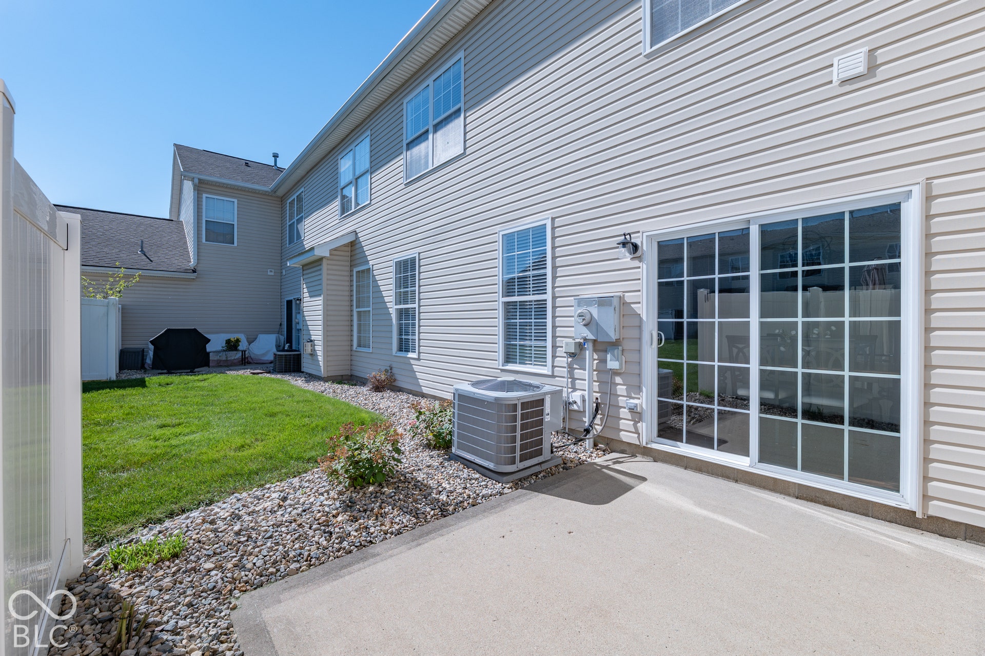 Sliding glass door with grid-patterned panes, concrete patio, vinyl siding, manicured lawn, and a white privacy fence