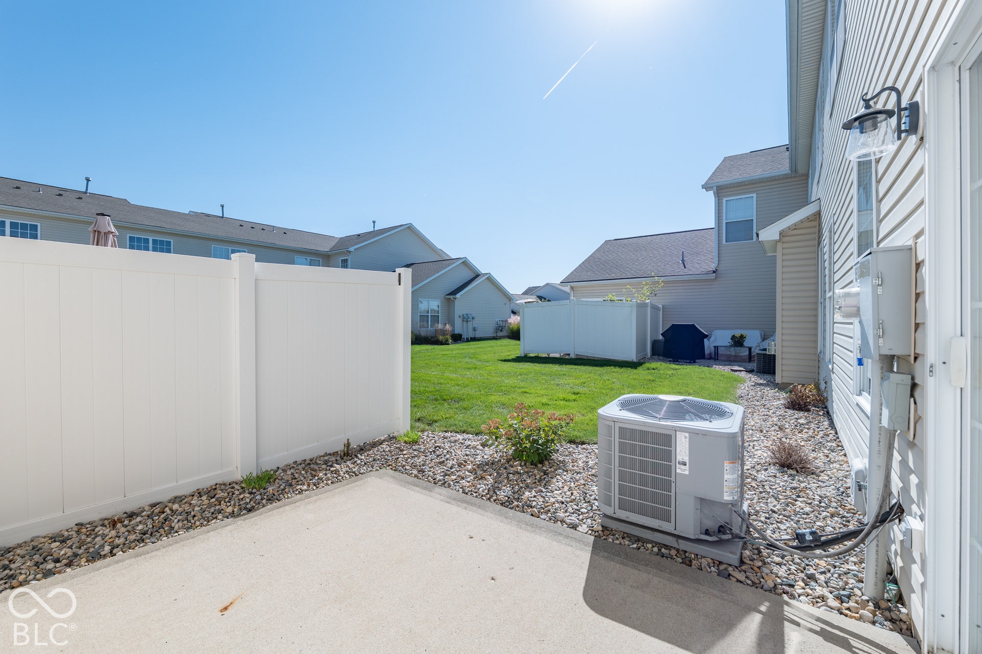 Concrete patio area featuring a white vinyl privacy fence, gravel landscaping, and exterior siding