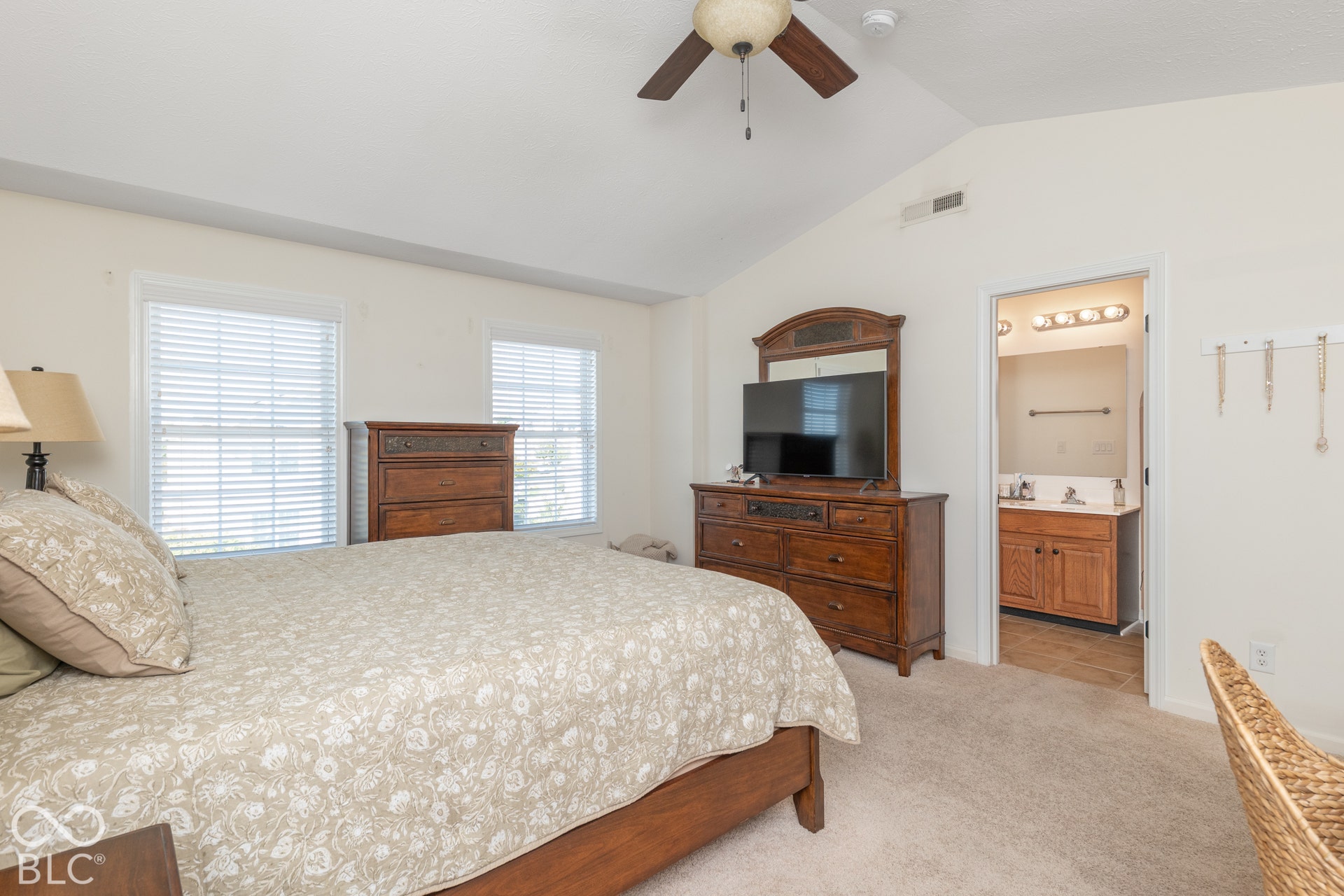 Vaulted ceiling with a ceiling fan, two windows, and neutral carpet flooring