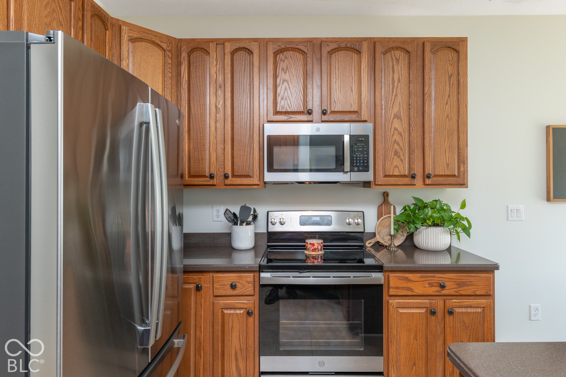 Stainless steel side-by-side refrigerator, stainless steel range, stainless steel microwave, wood-finish cabinetry, and dark countertops