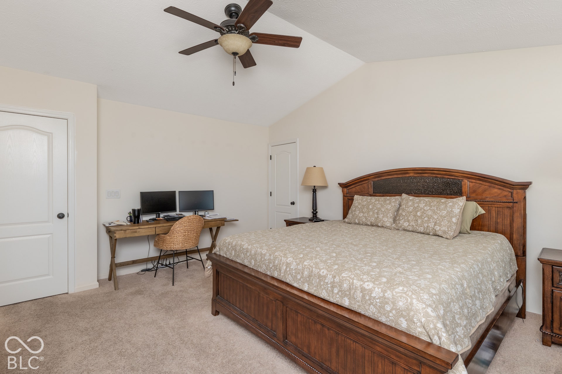 Vaulted ceiling with a ceiling fan, light-toned carpet flooring, white paneled doors, and a wood-finish bed frame with a detailed headboard