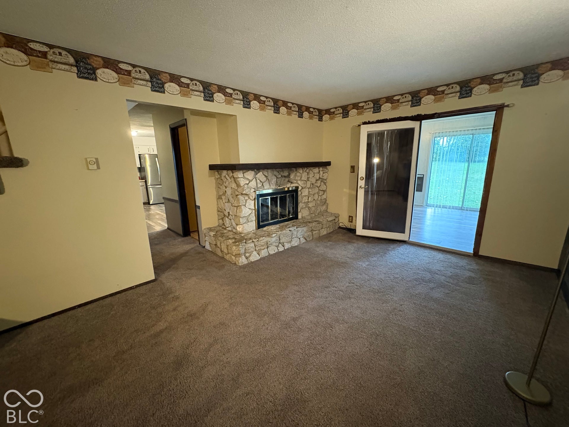 402 E Jackson Street, Farmland, IN 47340 Stone-clad fireplace with dark wood mantel, sliding glass door, and carpet flooring