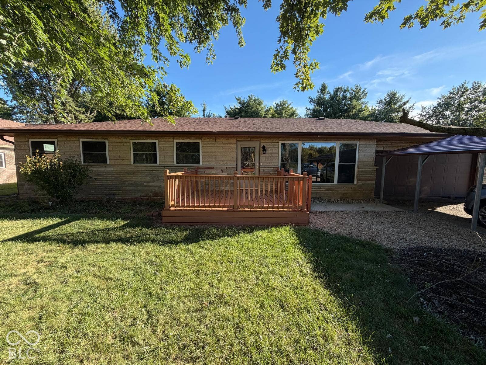 2819 E Edgewood Avenue, Indianapolis, IN 46227 Ranch-style exterior with stone veneer, an attached wood deck, multiple windows, and a detached metal carport