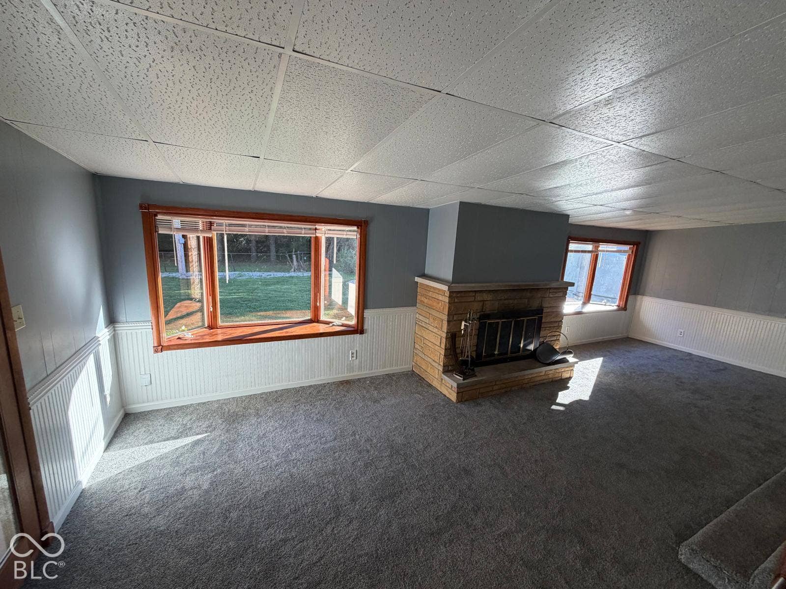 2819 E Edgewood Avenue, Indianapolis, IN 46227 Carpeted flooring, stone-front fireplace, wood-framed bay window, paneled wainscoting, and acoustic tile ceiling
