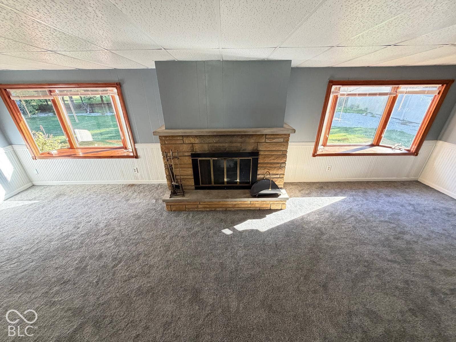2819 E Edgewood Avenue, Indianapolis, IN 46227 Stone-clad fireplace with a hearth, dual angled windows, textured ceiling, and wainscoting details