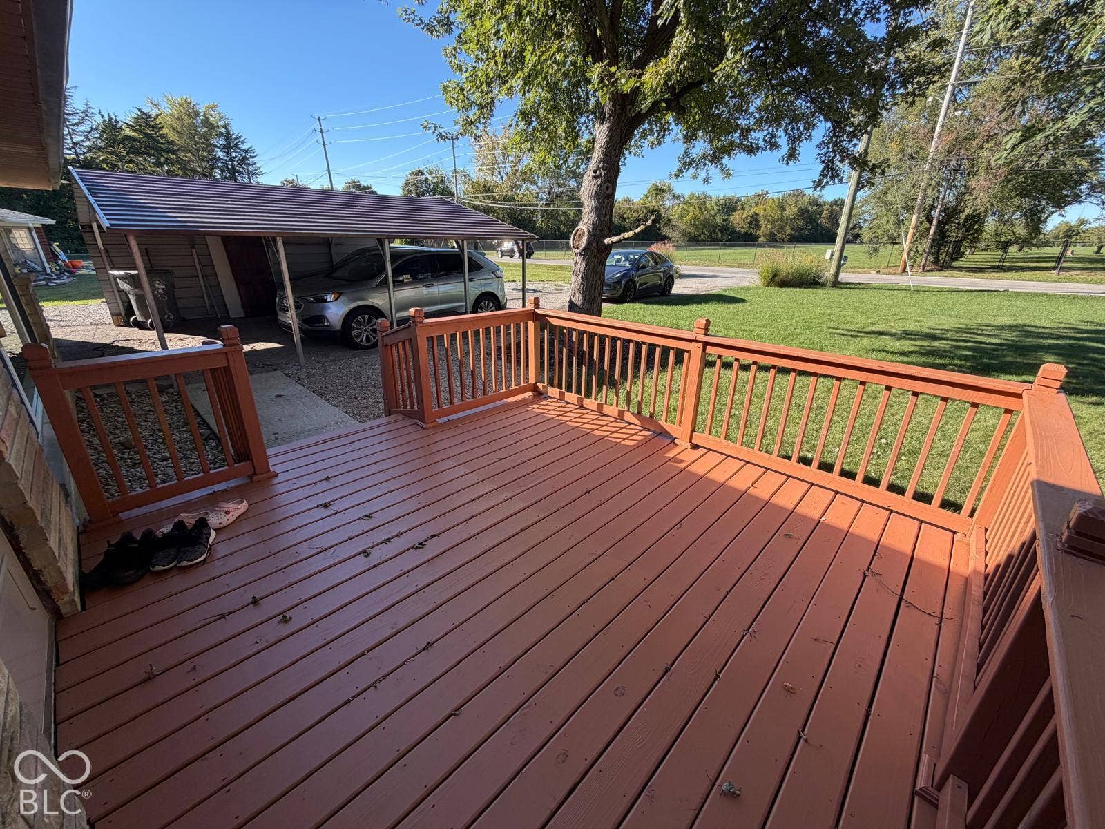 2819 E Edgewood Avenue, Indianapolis, IN 46227 Expansive wood deck with painted railings, featuring a gravel driveway and a metal-roofed carport