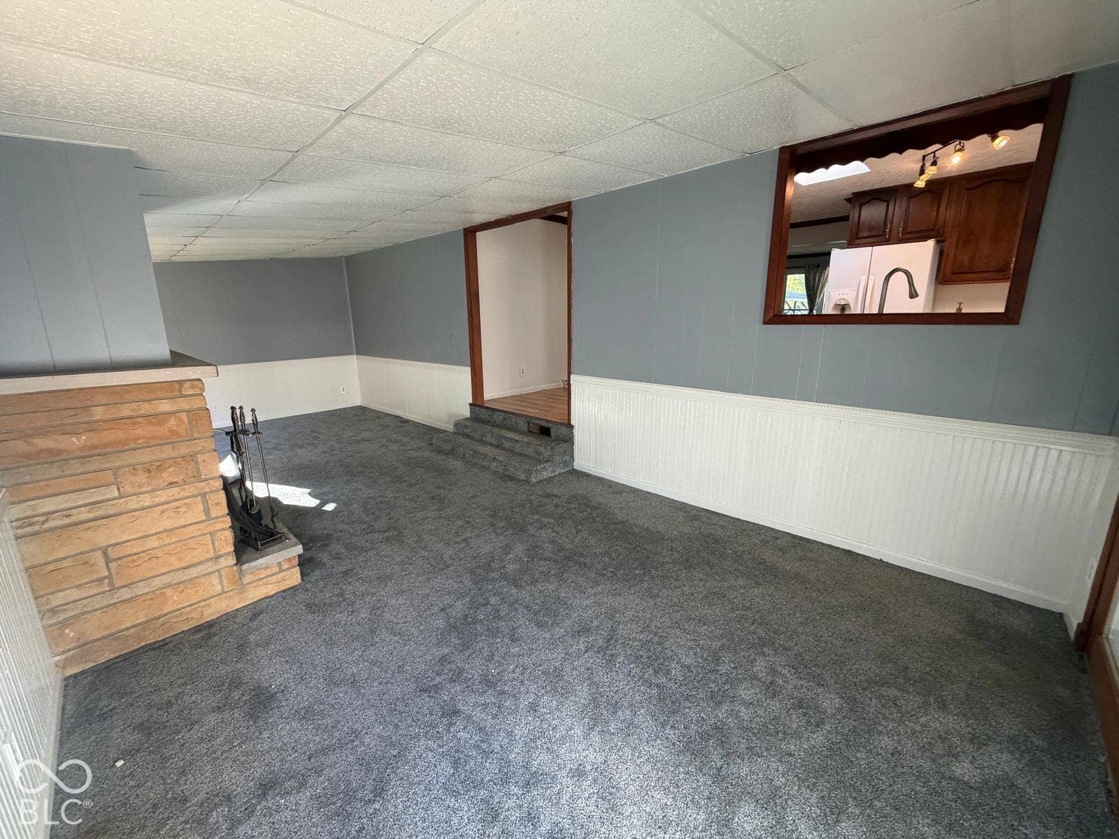 2819 E Edgewood Avenue, Indianapolis, IN 46227 Stone-clad fireplace with a hearth, gray carpeting, beadboard wainscoting, and a pass-through window with wood trim