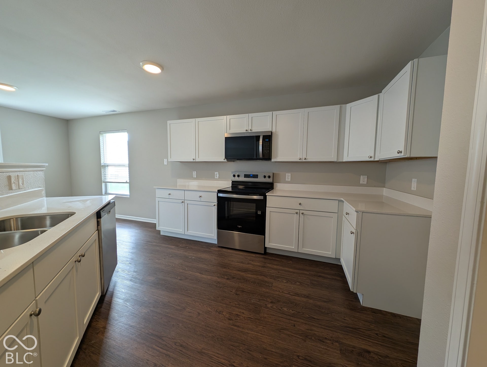 Kitchen featuring white cabinetry, stainless steel appliances, white countertops, a double basin sink, and wood-finish flooring