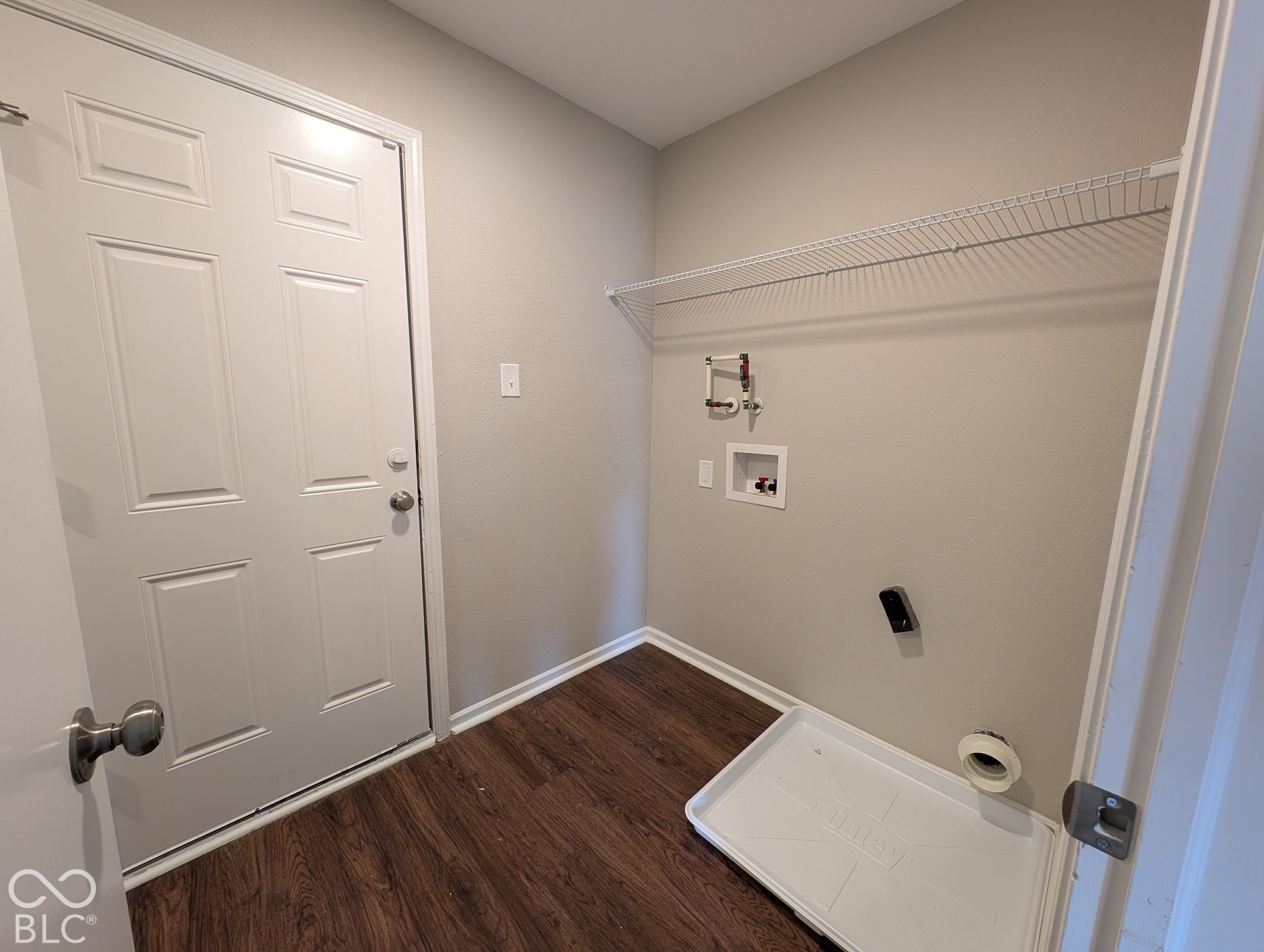 Laundry area featuring wood-finish flooring, light neutral wall paint, a wire shelf, and a panel door