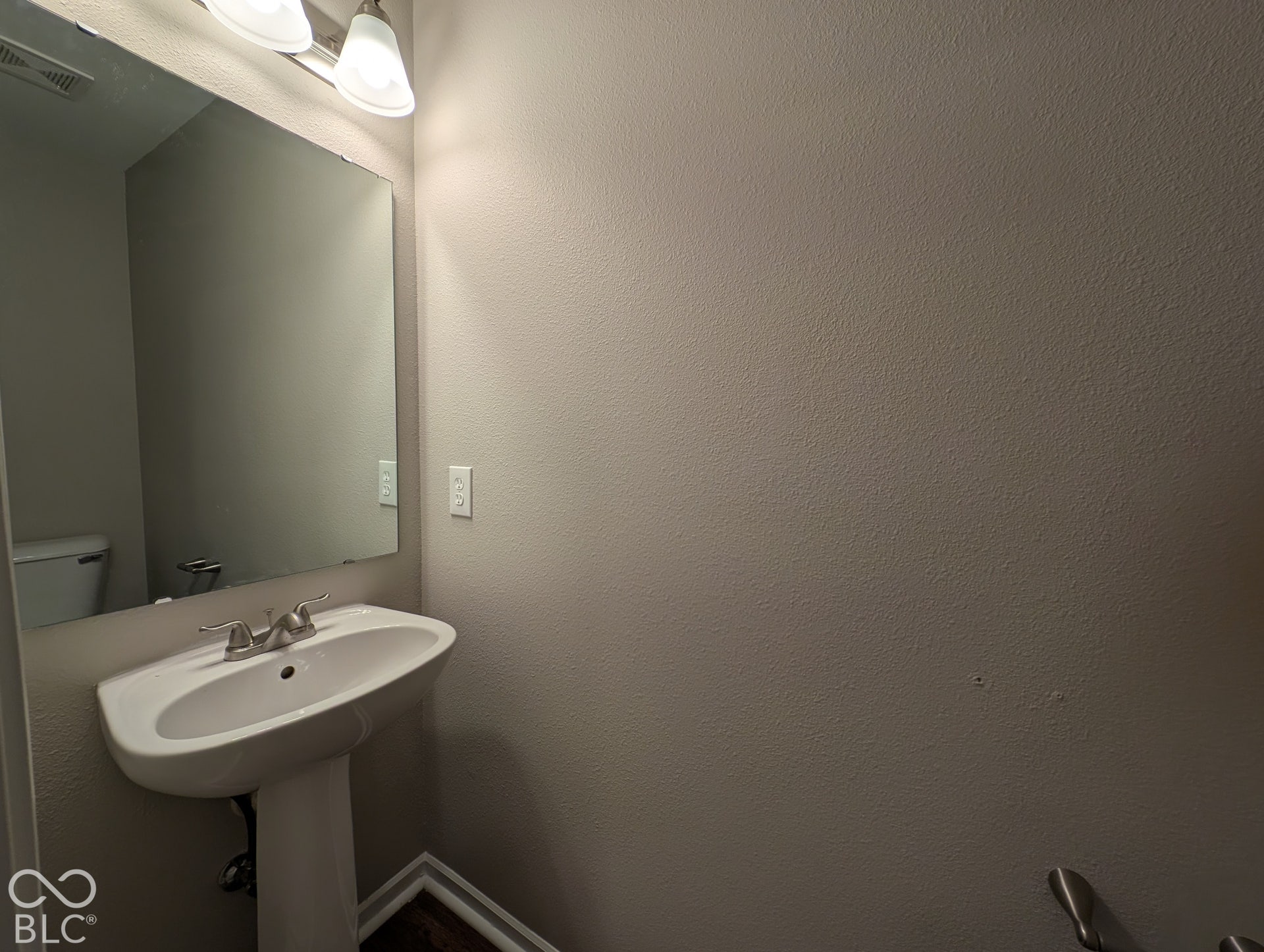 Pedestal sink with chrome-finish faucet, rectangular wall-mounted mirror, and wall-mounted light fixture with frosted glass shades