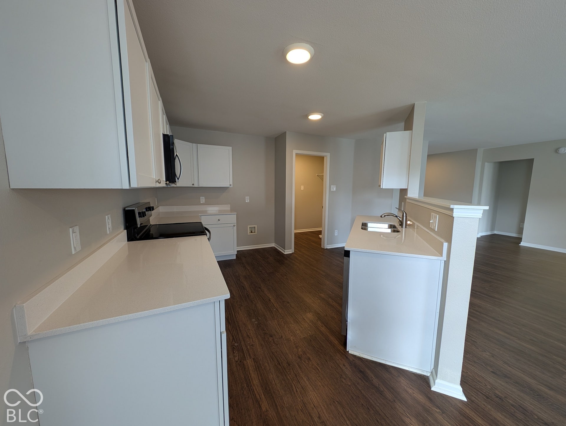 White cabinetry, light-toned countertops, stainless steel sink, black electric range, and wood-finish flooring