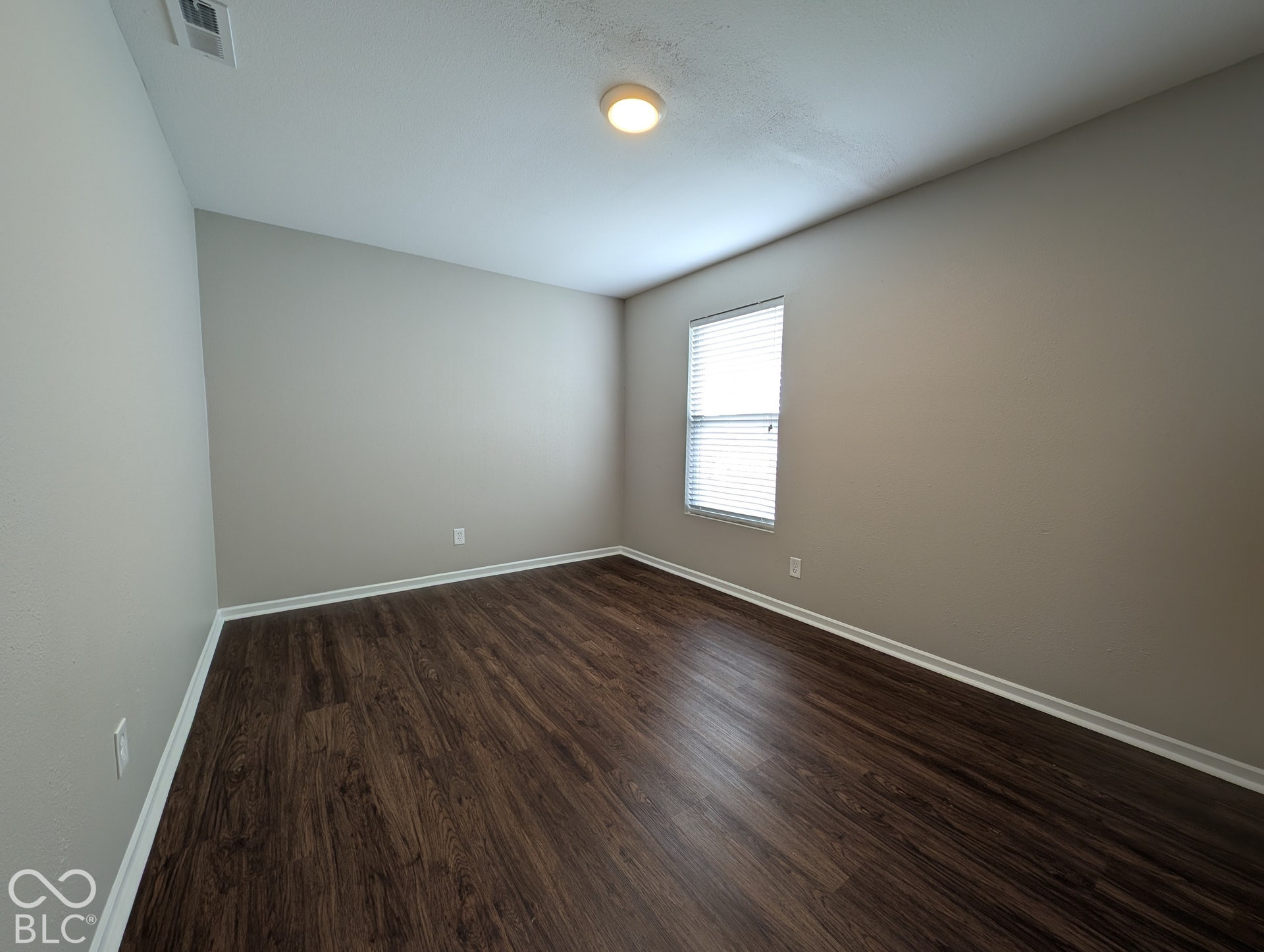 Wood-finish flooring, neutral wall paint, overhead lighting, window with blinds, and white trim