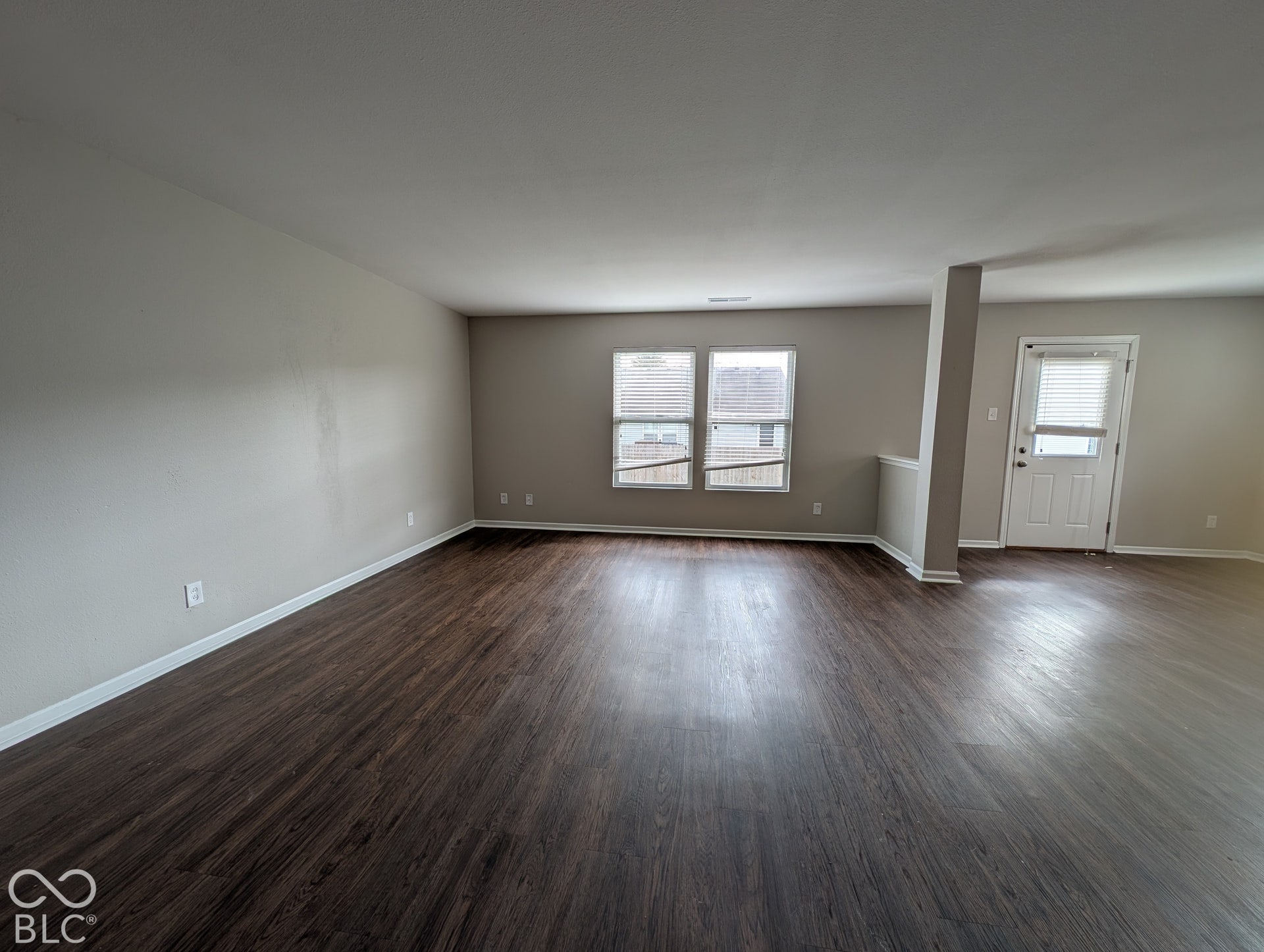 Expansive room featuring wood-finish flooring, neutral wall tones, two paneled windows, and a paneled exterior door