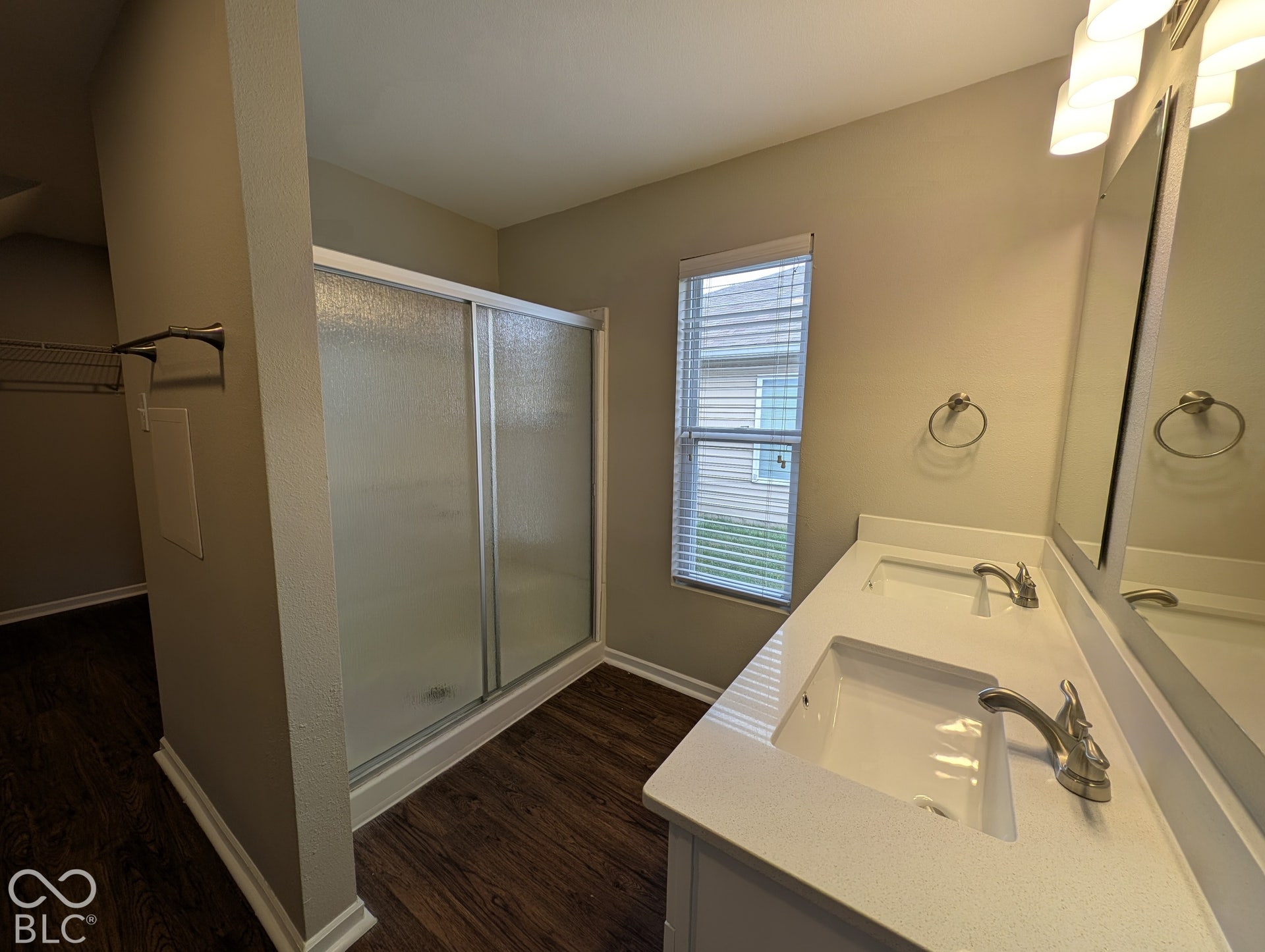 Double vanity with integrated sinks, brushed nickel fixtures, wood-finish flooring, and a frosted glass shower enclosure