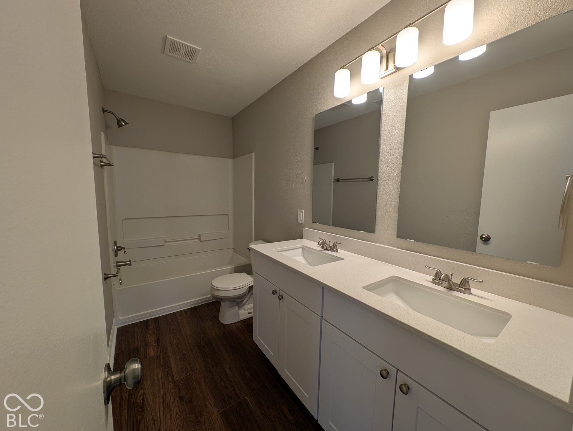Double vanity with white cabinetry, integrated sinks, white countertops, and wood-finish flooring