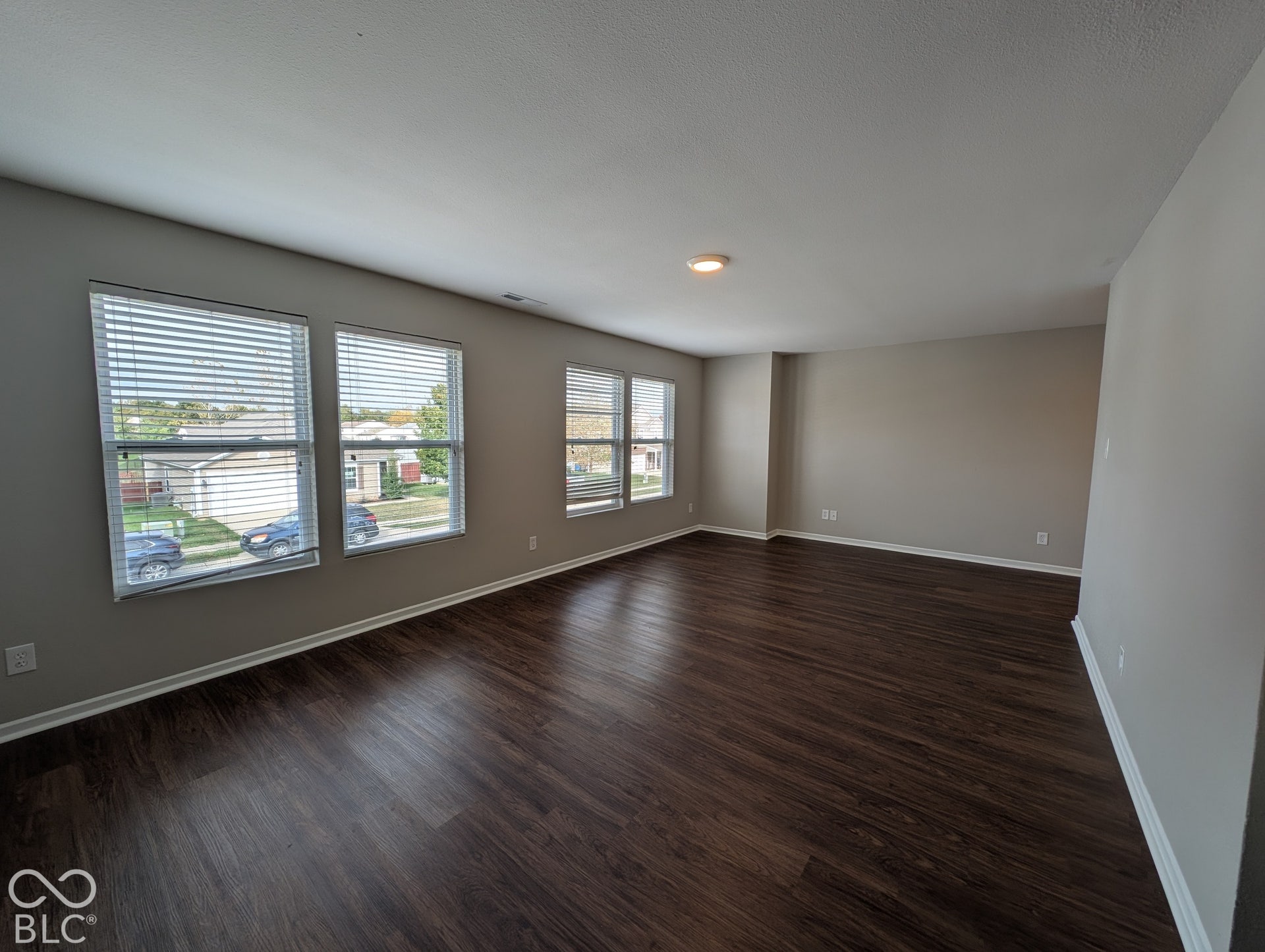 Spacious room featuring wood-finish flooring, multiple windows with blinds, neutral wall tones, and overhead lighting
