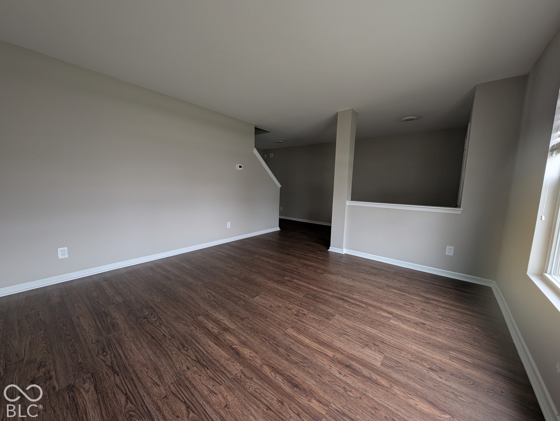 Spacious room featuring wood-finish flooring, light neutral wall paint, and a window with vertical blinds