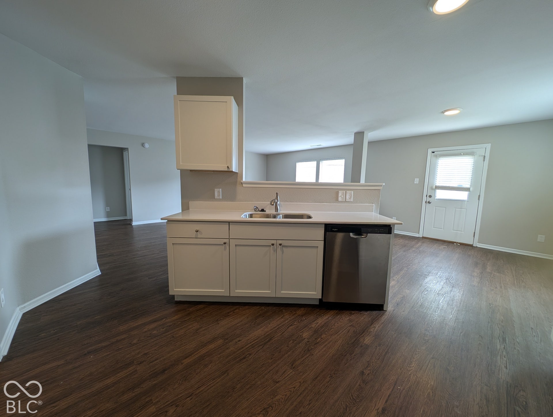 Kitchen island with a stainless steel sink and integrated dishwasher, white cabinetry, light-toned countertops, and wood-finish flooring