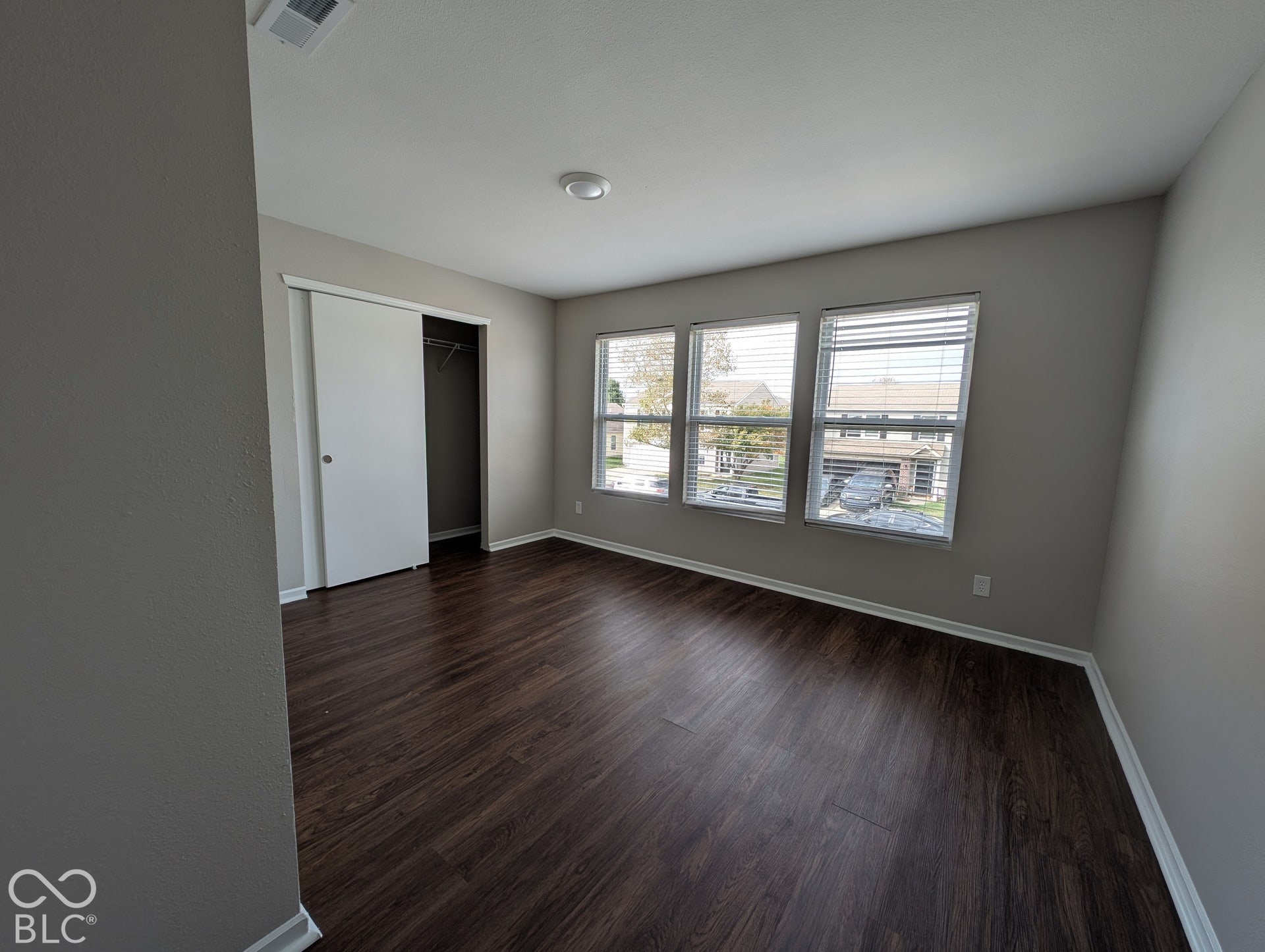 Dark wood-finish flooring, sliding closet door, and three windows with blinds