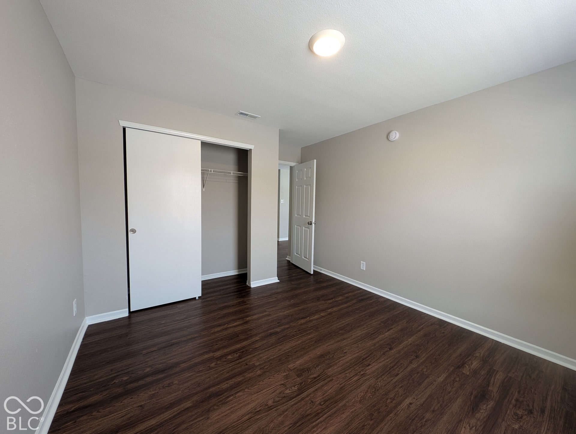 Wood-finish flooring, neutral wall paint, overhead flush-mount lighting, sliding closet doors, and white trim