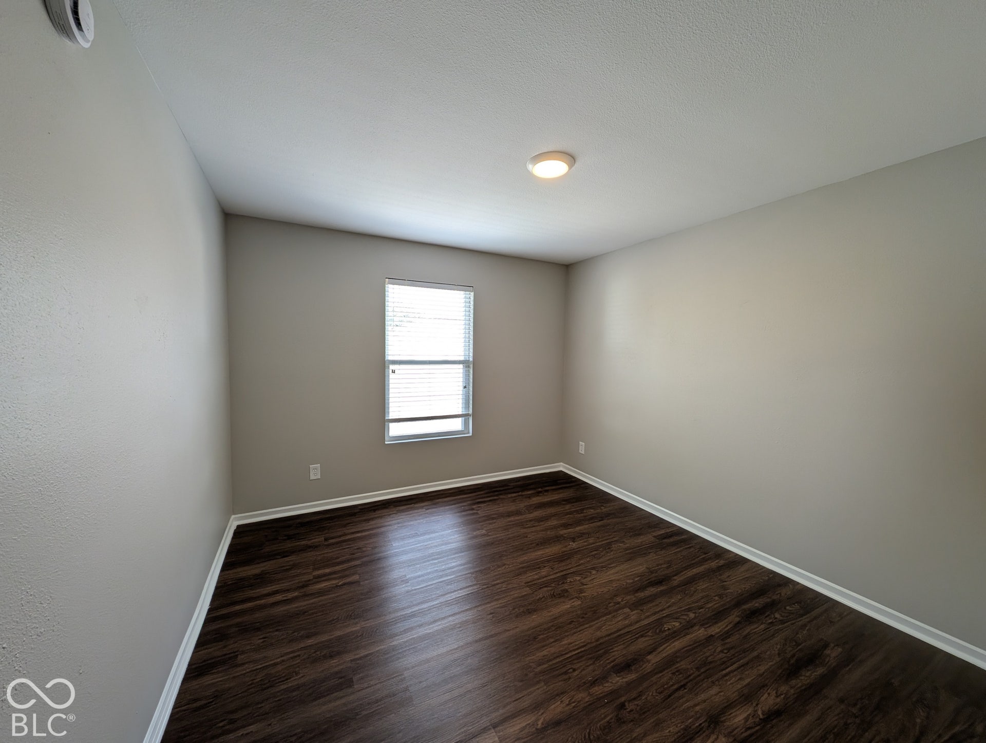 Wood-finish flooring, neutral wall tones, window with blinds, and a flush-mount ceiling light