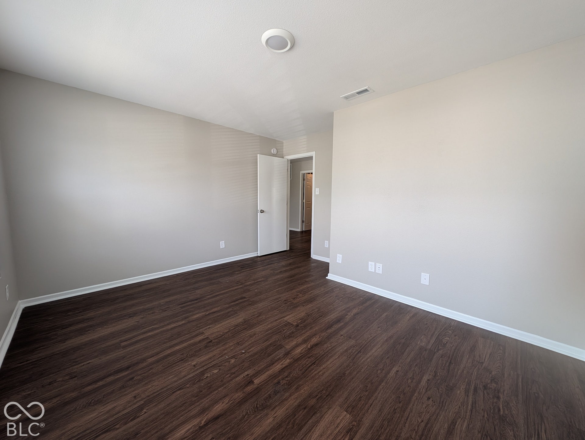 Wood-finish flooring, neutral wall tones, recessed ceiling lighting, and a white interior door