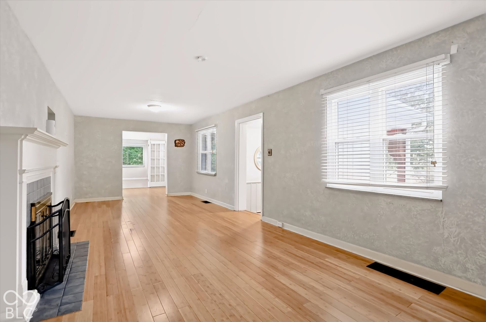Hardwood-finish flooring, a fireplace with a tile surround and white mantel, and a window with blinds