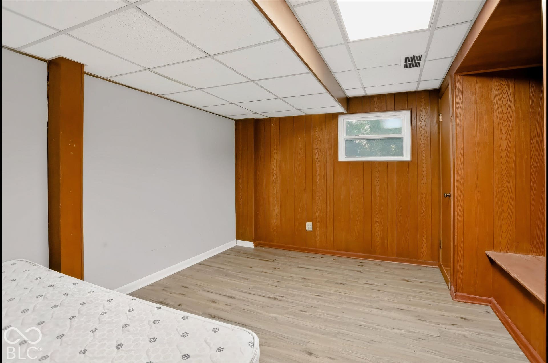 Wood-finish flooring, wood paneling, drop ceiling with integrated lighting, and a window