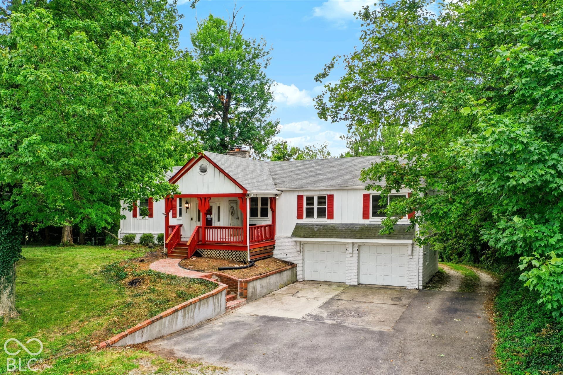 White exterior with red trim and shutters, covered front porch, attached two-car garage, and established trees