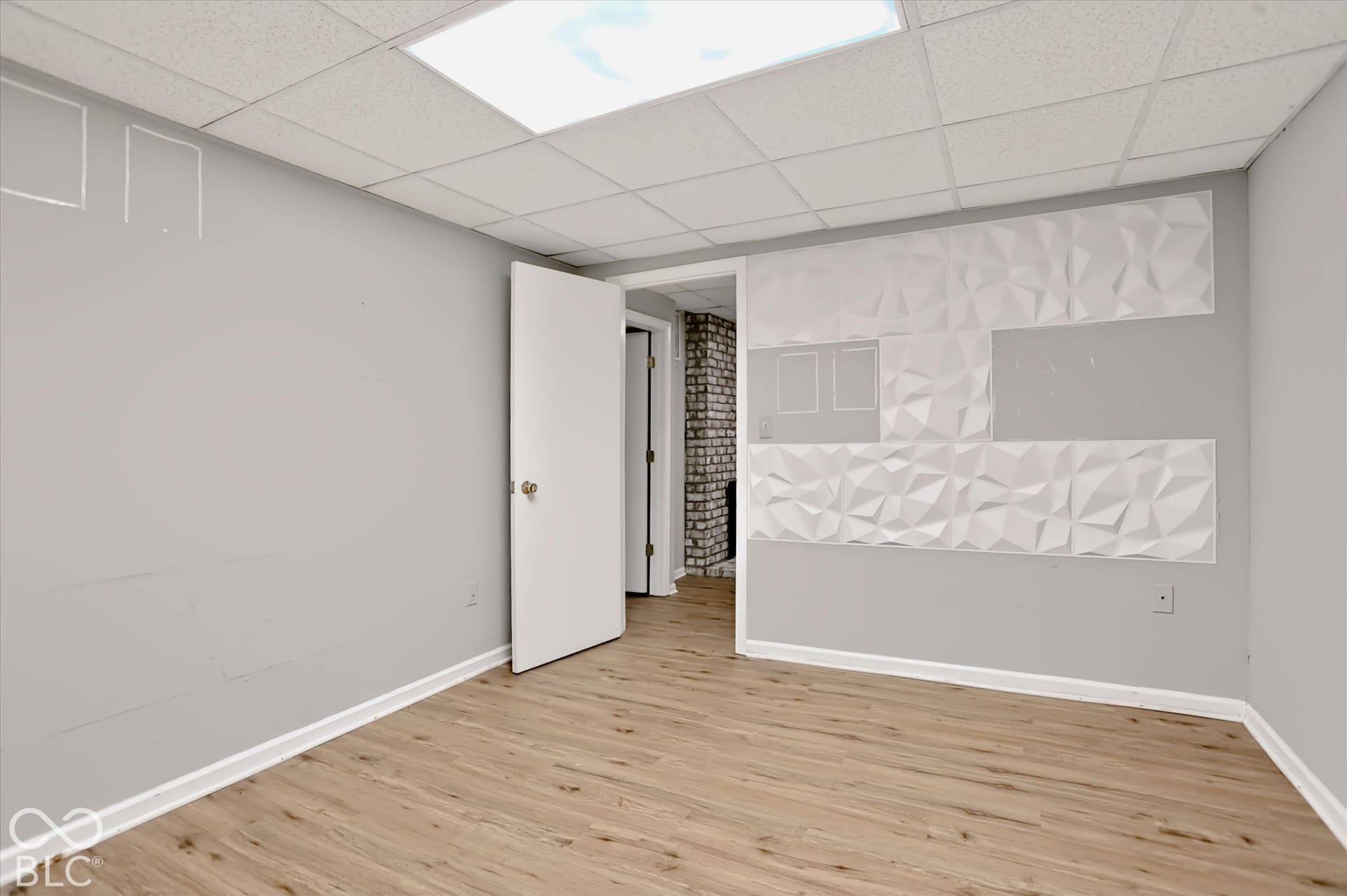 Wood-finish flooring, drop-tile ceiling with recessed lighting, and a decorative textured wall panel