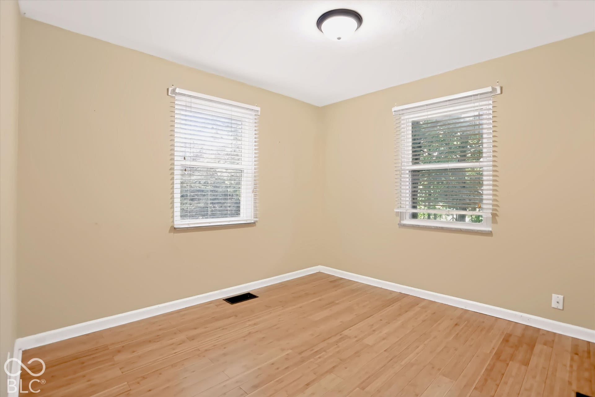 Wood-finish flooring, neutral wall tones, two windows with blinds, and a ceiling-mounted light fixture