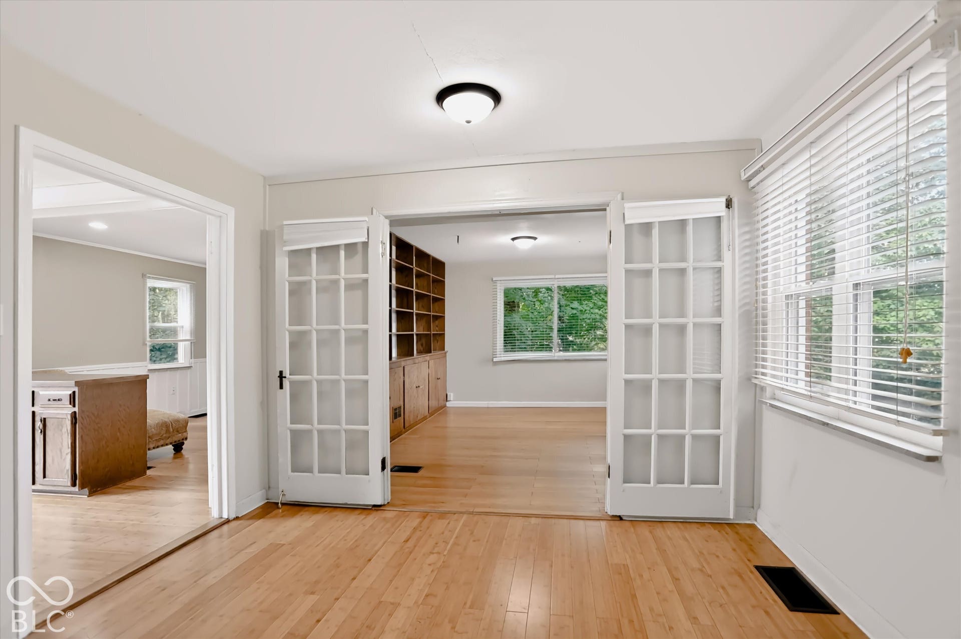 Hardwood-style flooring throughout, French doors with glass panels, built-in shelving, recessed lighting, and a window with blinds
