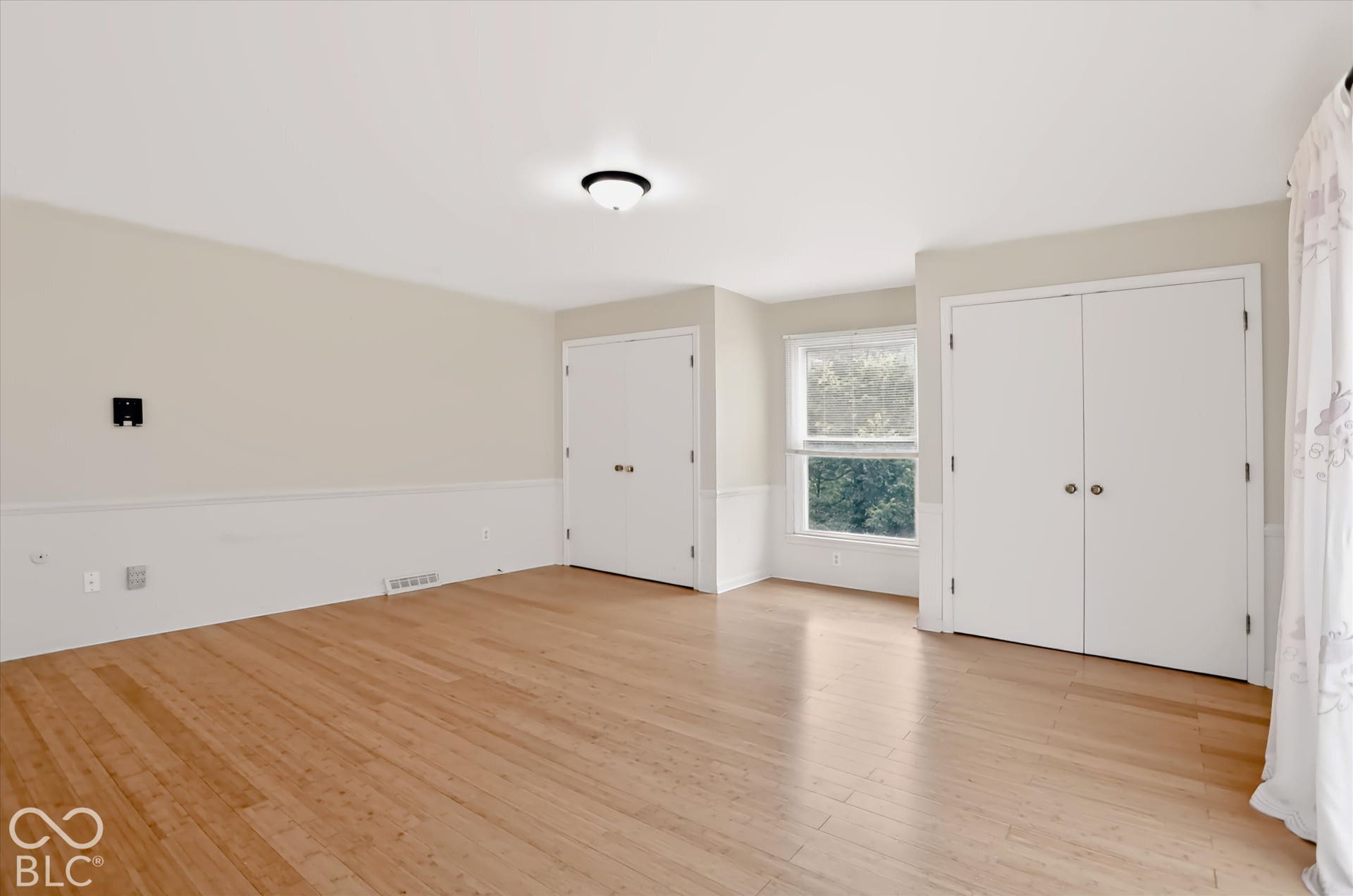 Hardwood flooring, painted walls with wainscoting, recessed window, and two sets of double-door closets