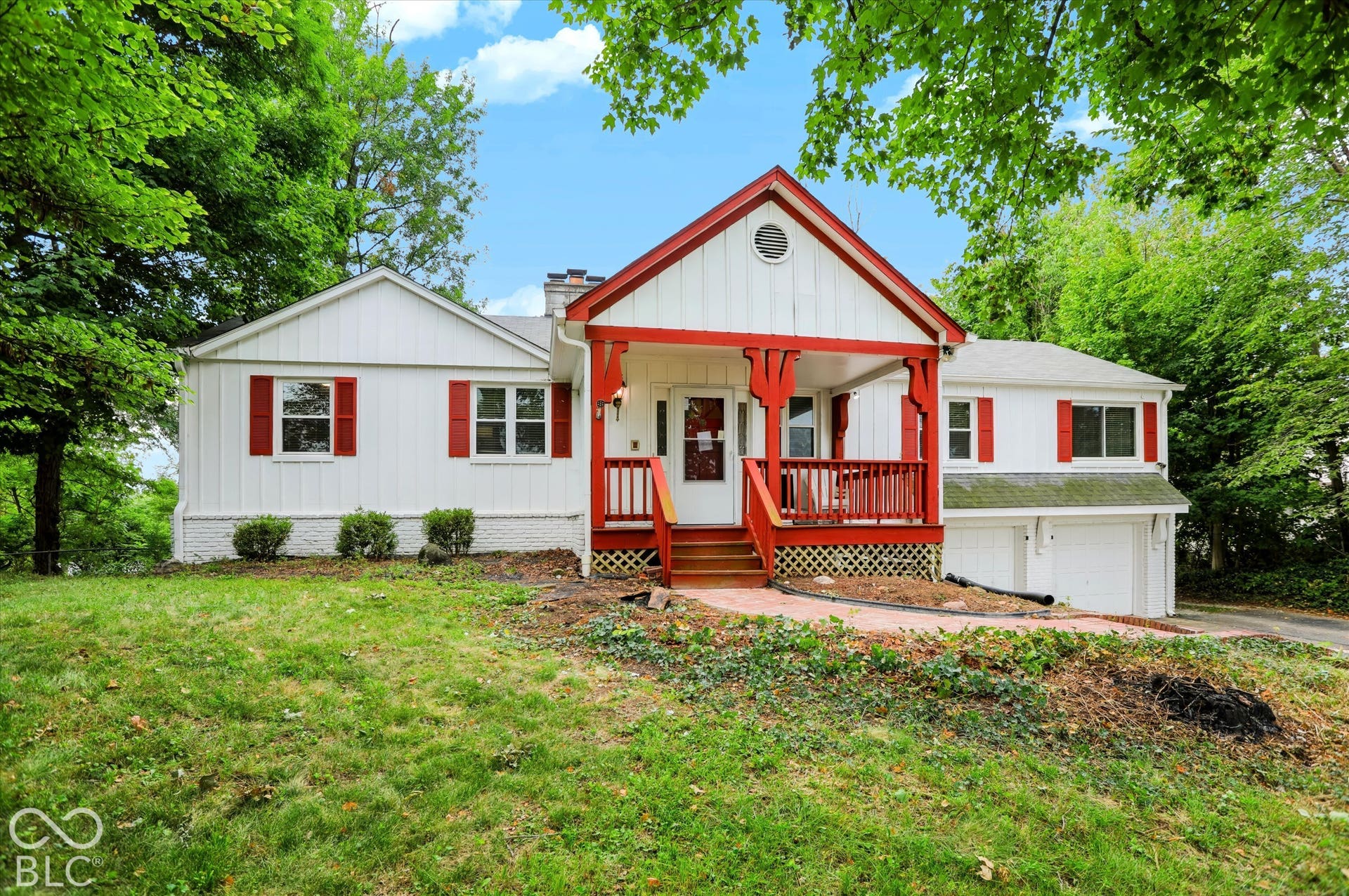 White exterior with red trim, covered front porch, white garage doors, and a brick-paved walkway