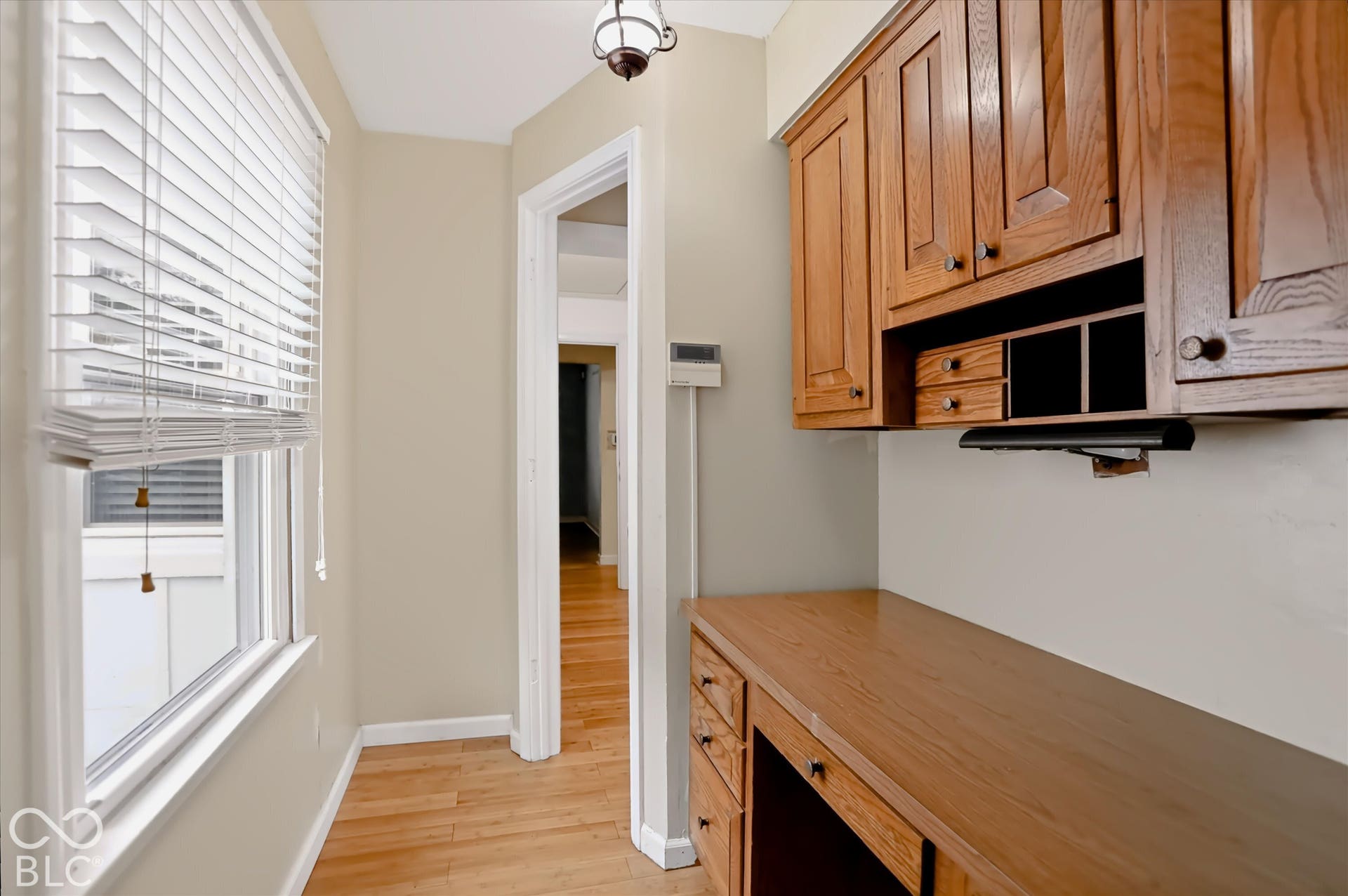 Built-in desk with wood-finish cabinetry, wood-finish flooring, and a window with blinds