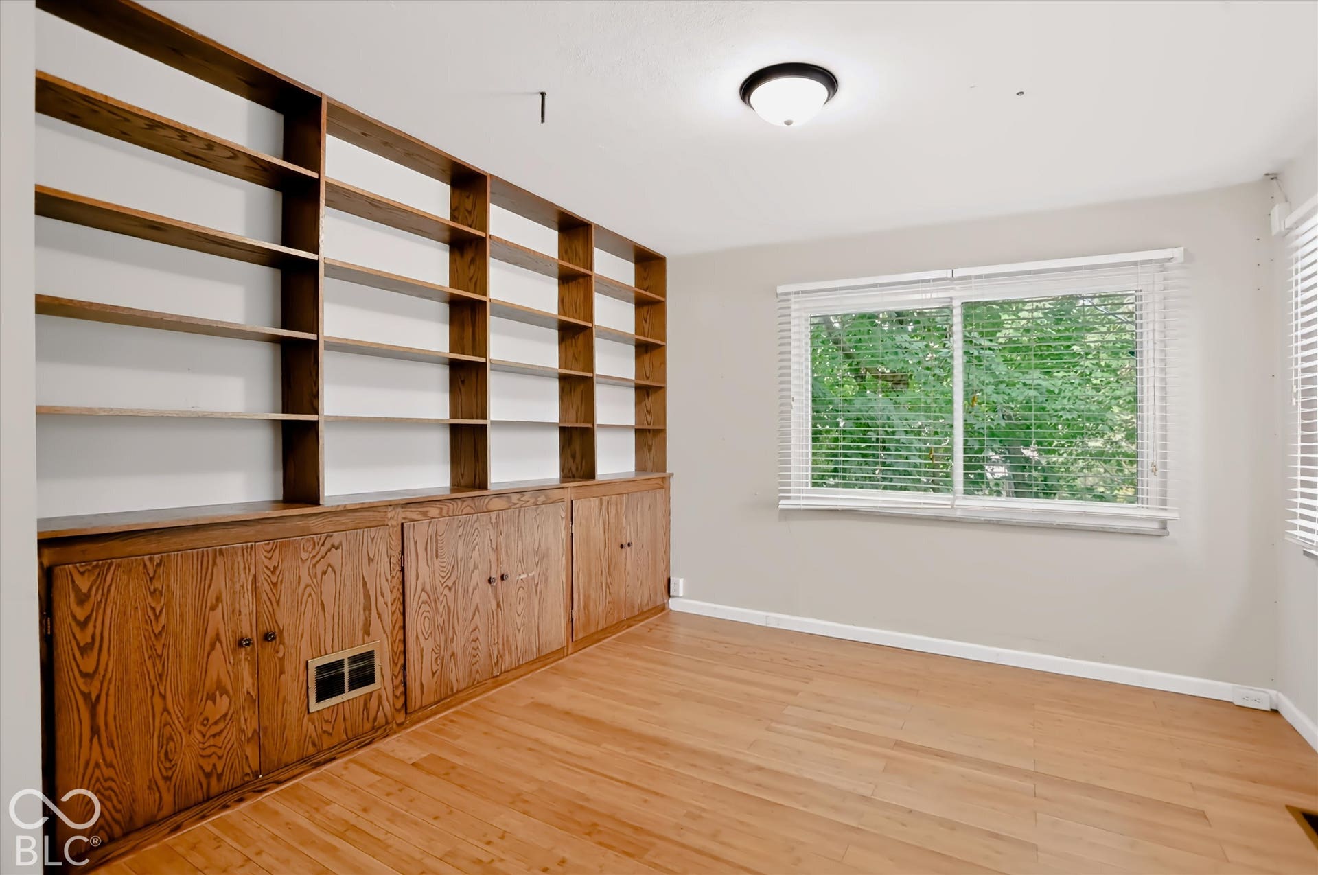 Built-in wood shelving with lower cabinetry, wood-finish flooring, and a window with blinds