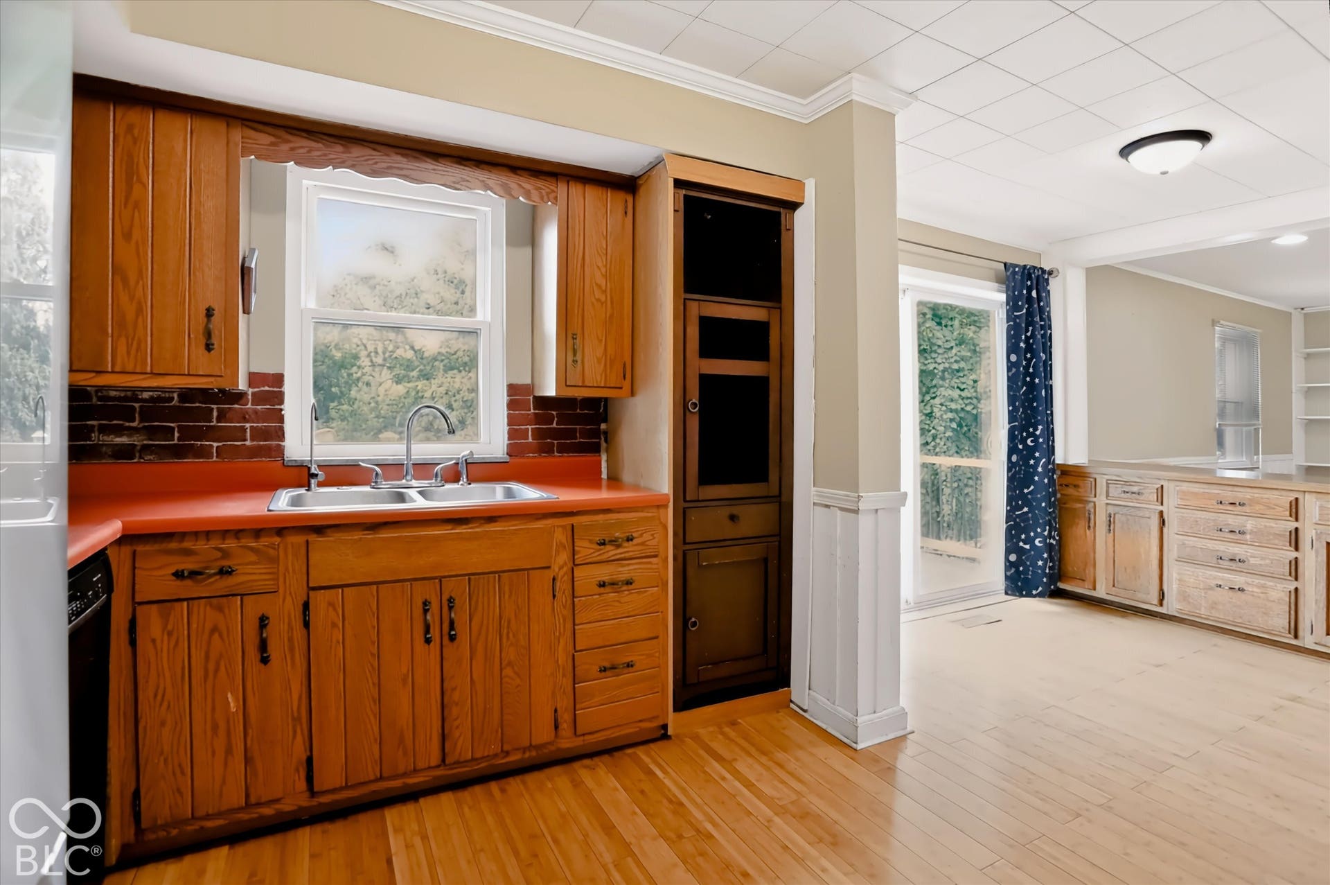 Kitchen featuring wood cabinetry, a double basin stainless steel sink, brick-look backsplash, and wood-finish flooring
