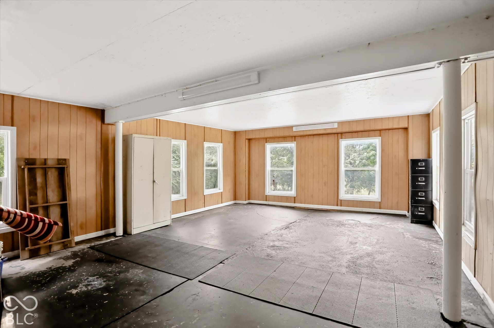 Room with wood-panel walls, multiple windows, and exposed support beams